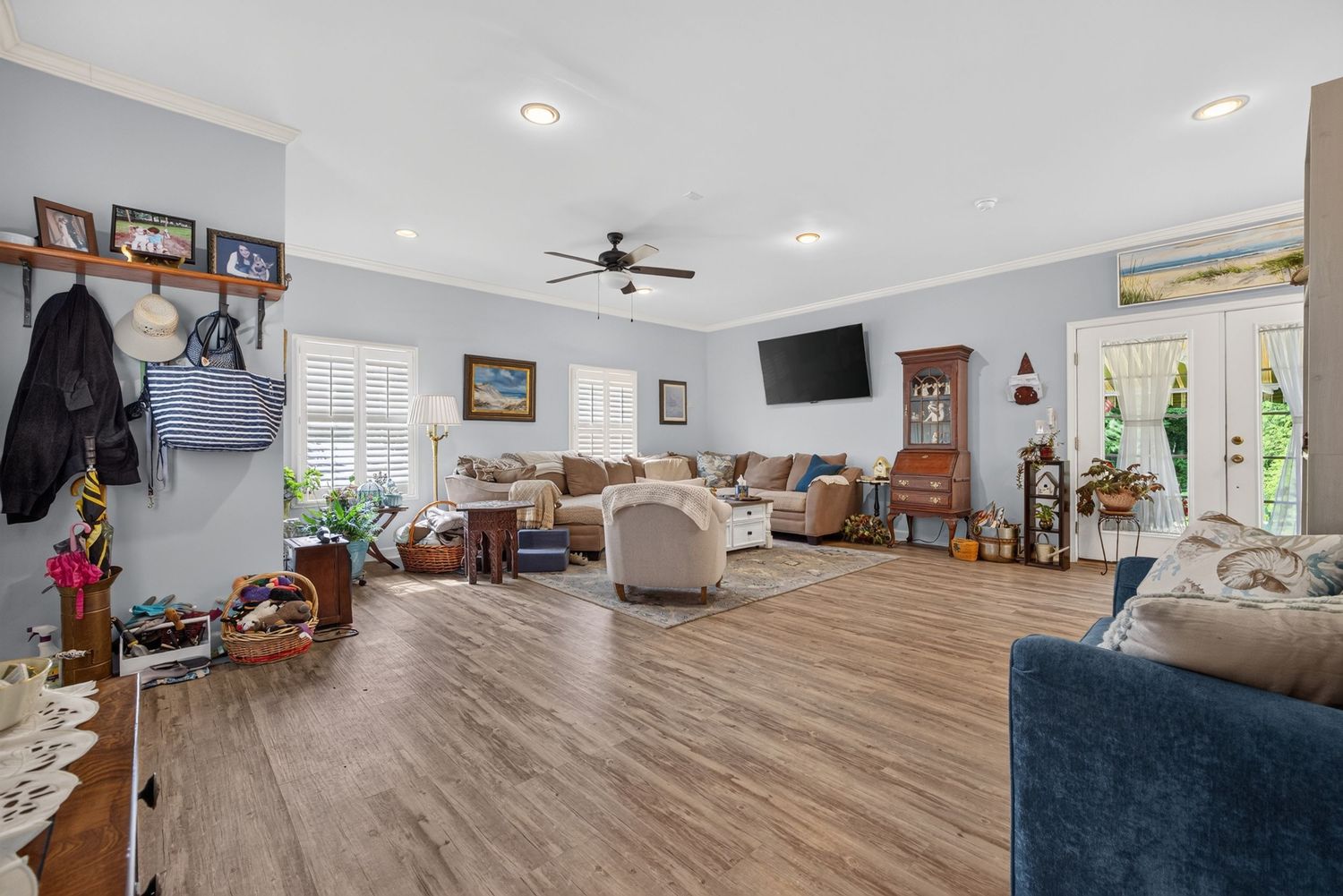 Spacious living room with hardwood floors, ceiling fan, wall-mounted TV, neutral decor, and French doors leading to a bright outdoor area.