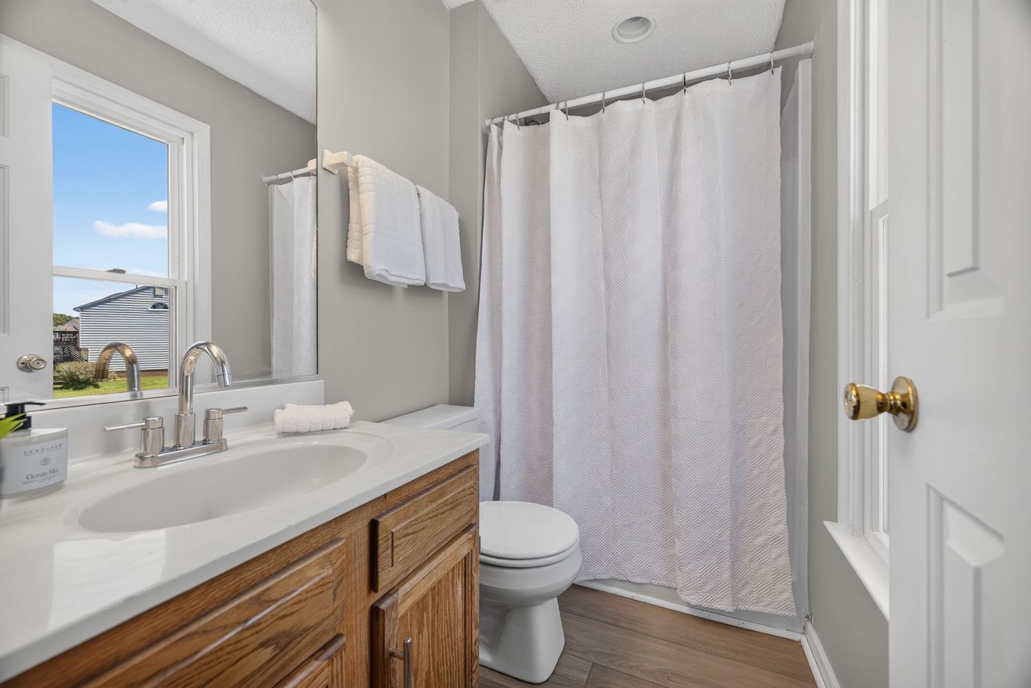 Clean bathroom with wood vanity, white quartz countertop, shower with curtain, toilet, and hardwood floors.