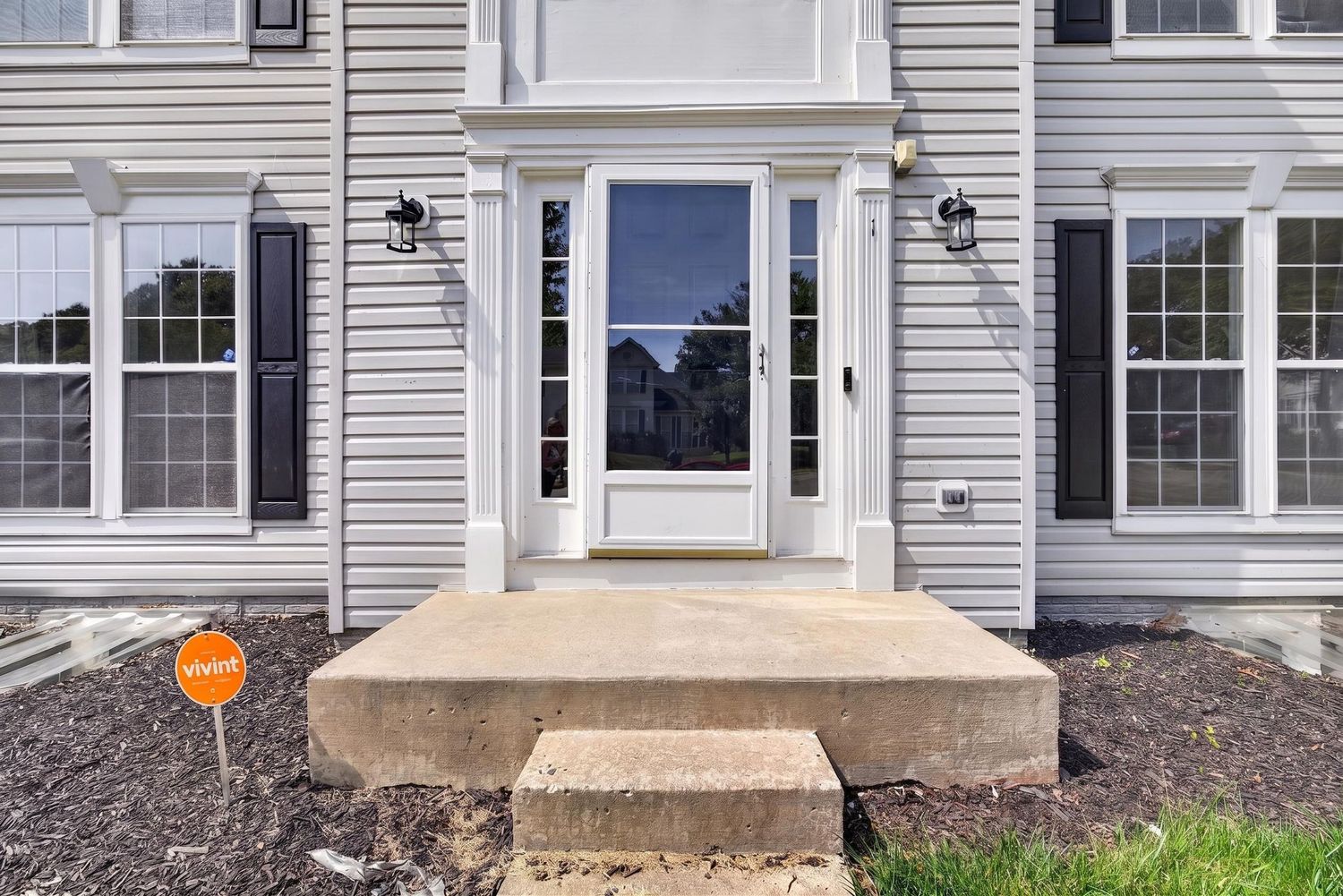 Gray colonial home exterior featuring a white front door with sidelights, concrete steps, and black wall lanterns.