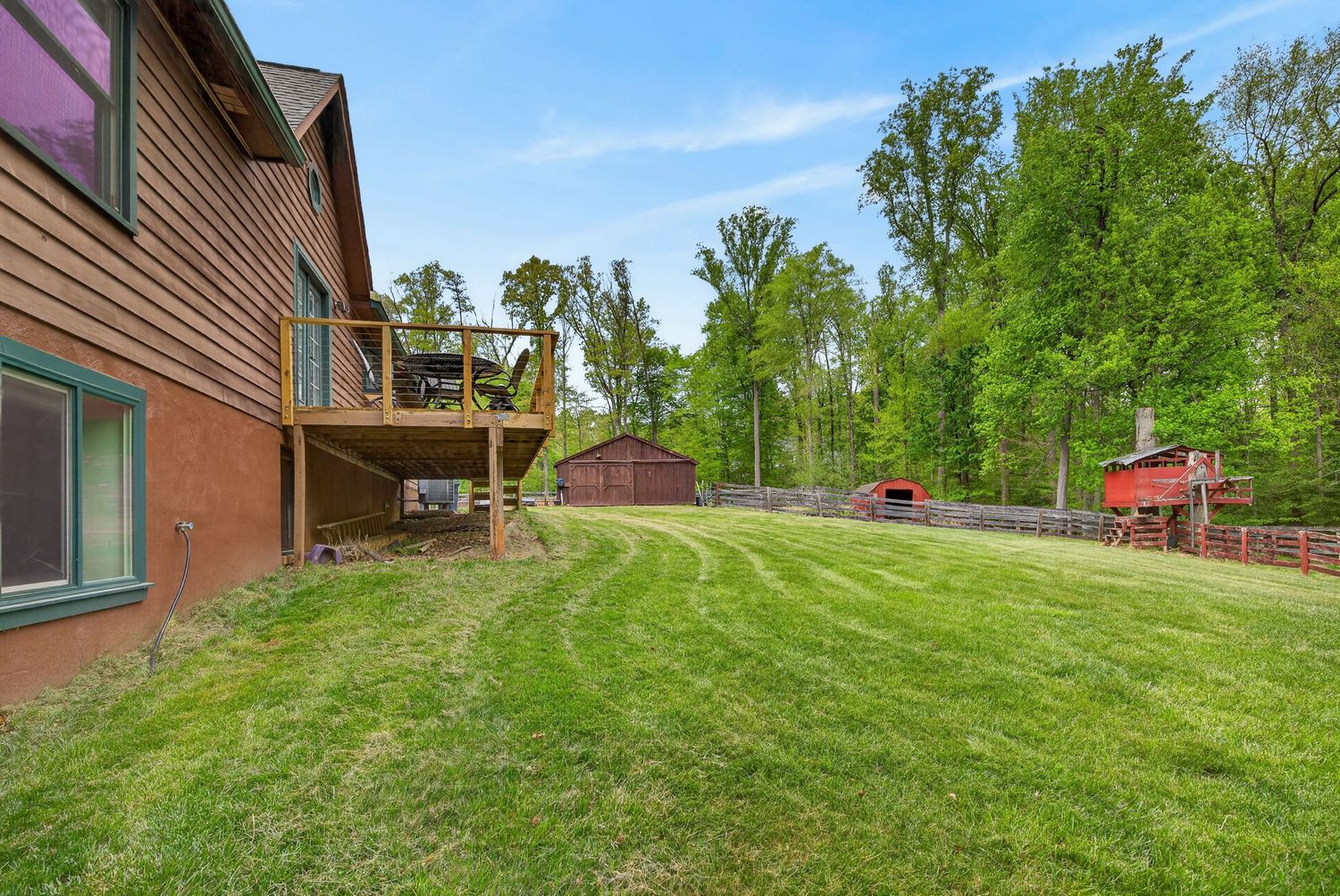 Spacious backyard with lush green lawn, wooden deck, and surrounding trees on a sunny day.