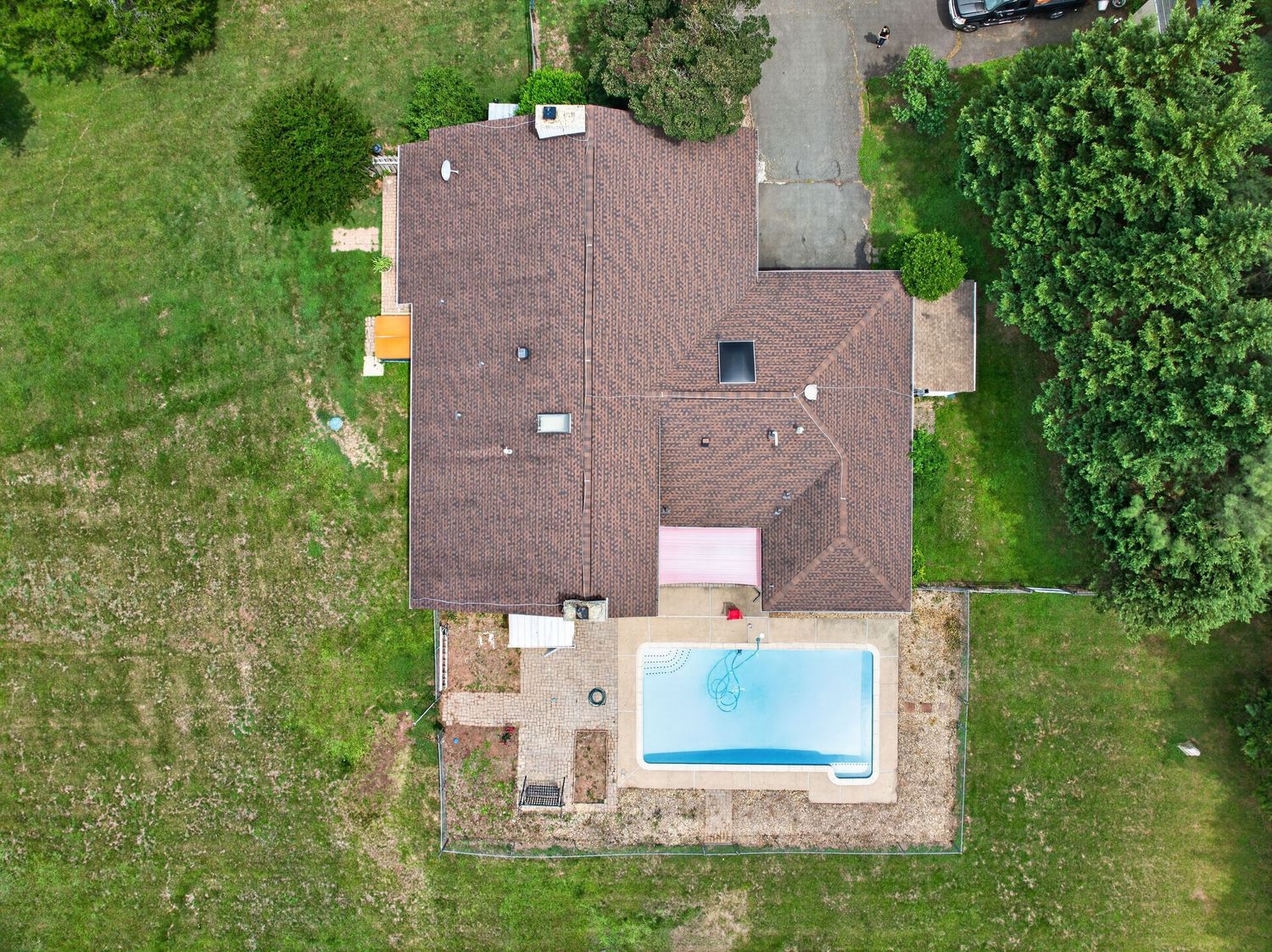 Aerial view of a residential home with a brown roof, backyard swimming pool, and surrounding green lawn and trees.