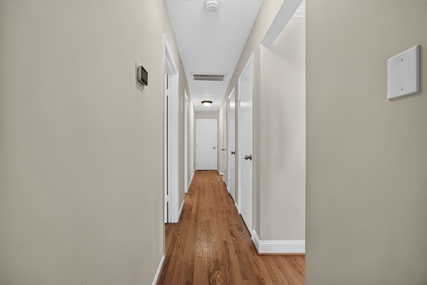 Bright hallway with white walls, white trim doors, and warm hardwood floors leading to multiple rooms.