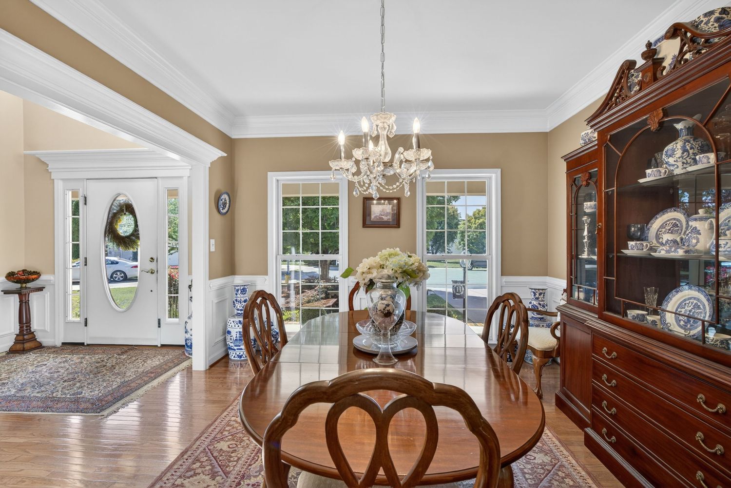 Elegant dining room with chandelier, mahogany furniture, china cabinet, and French doors leading to a bright sunlit exterior.