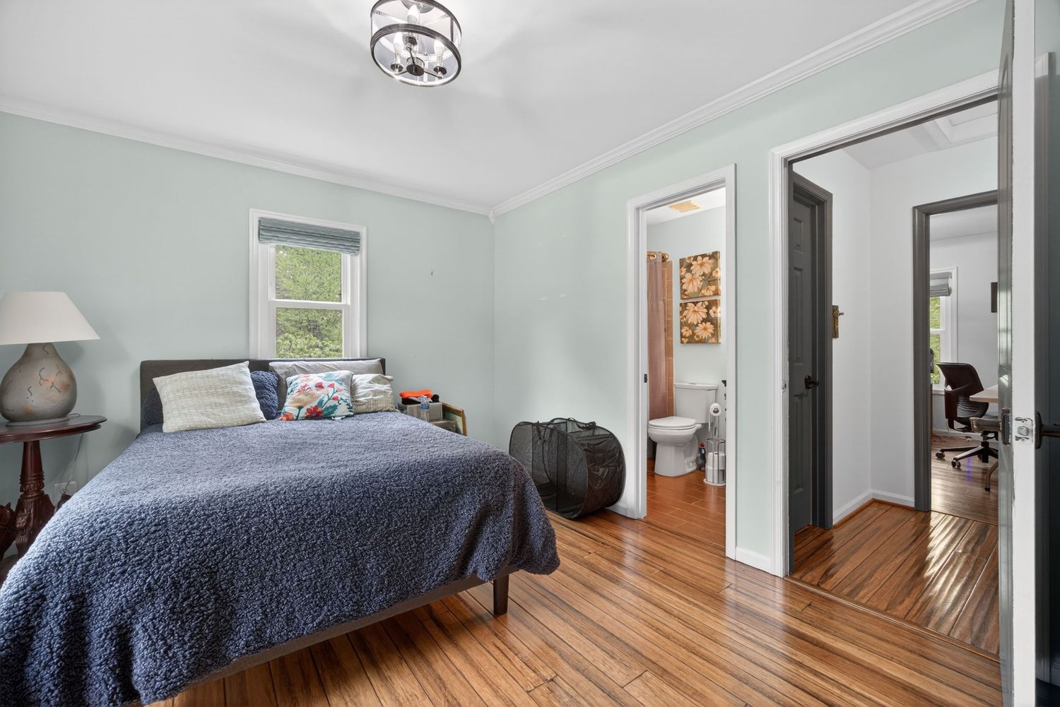 Bright bedroom with hardwood floors, blue bedding, crown molding, ensuite bathroom, and a chandelier in a classic home.