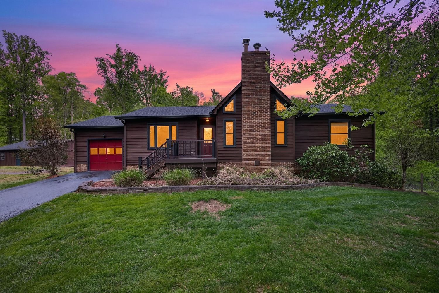 Charming wood cabin home with red garage door and covered porch glowing under a vibrant pink and purple sunset sky.