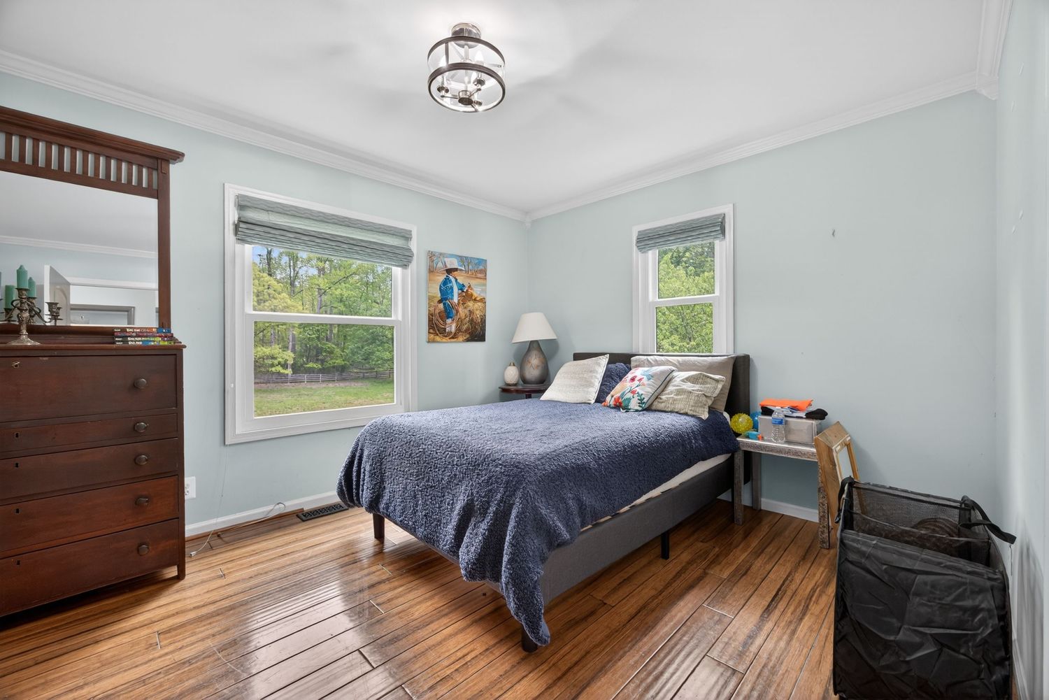 Bright bedroom with hardwood floors, blue bedspread, crown molding, and natural light from two windows.
