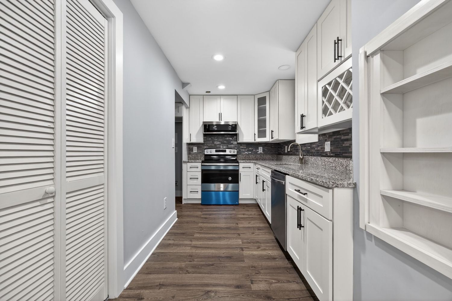 Modern kitchen with white cabinets, granite countertops, stainless steel appliances, and dark hardwood floors.