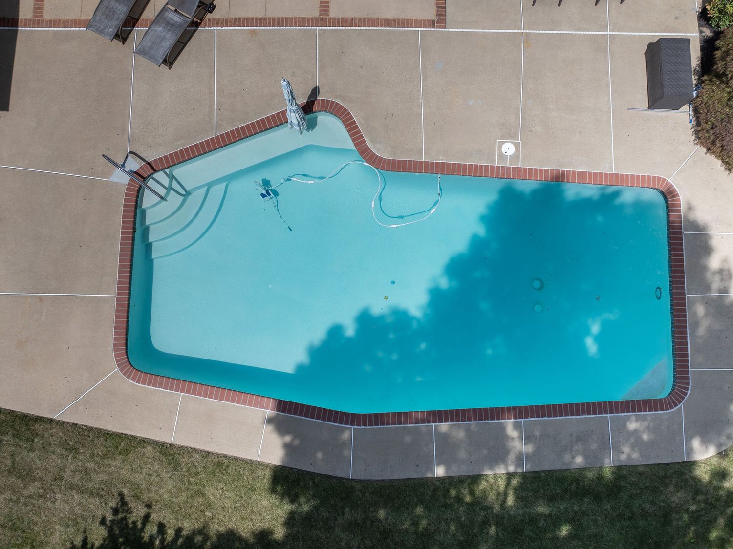Aerial view of a freeform backyard swimming pool with turquoise water surrounded by a brick-edged concrete patio.