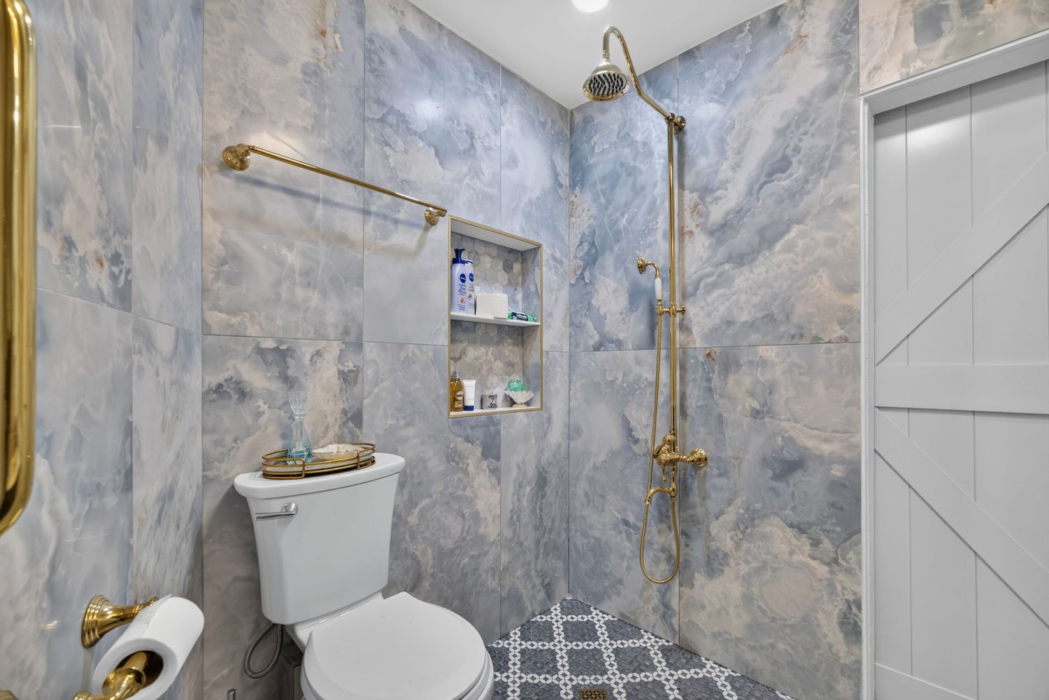 Luxurious bathroom with blue marble walls, gold fixtures, walk-in shower, mosaic tile floor, and built-in niche shelving.