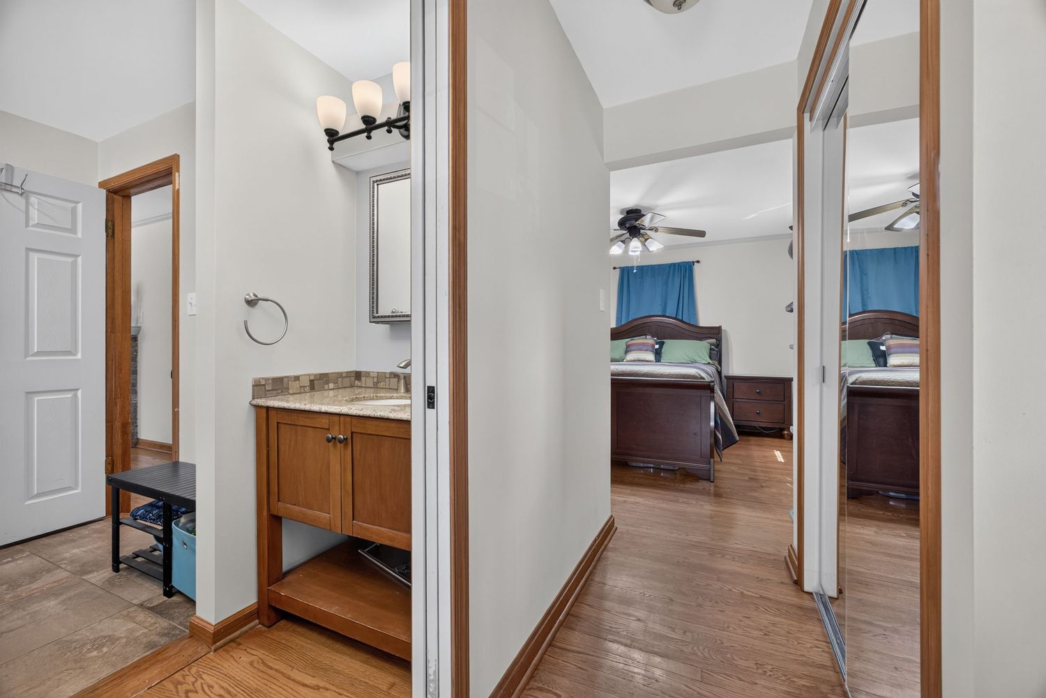 Hallway with hardwood floors leading to a bedroom, featuring a wooden vanity with sink and mirror on the left.