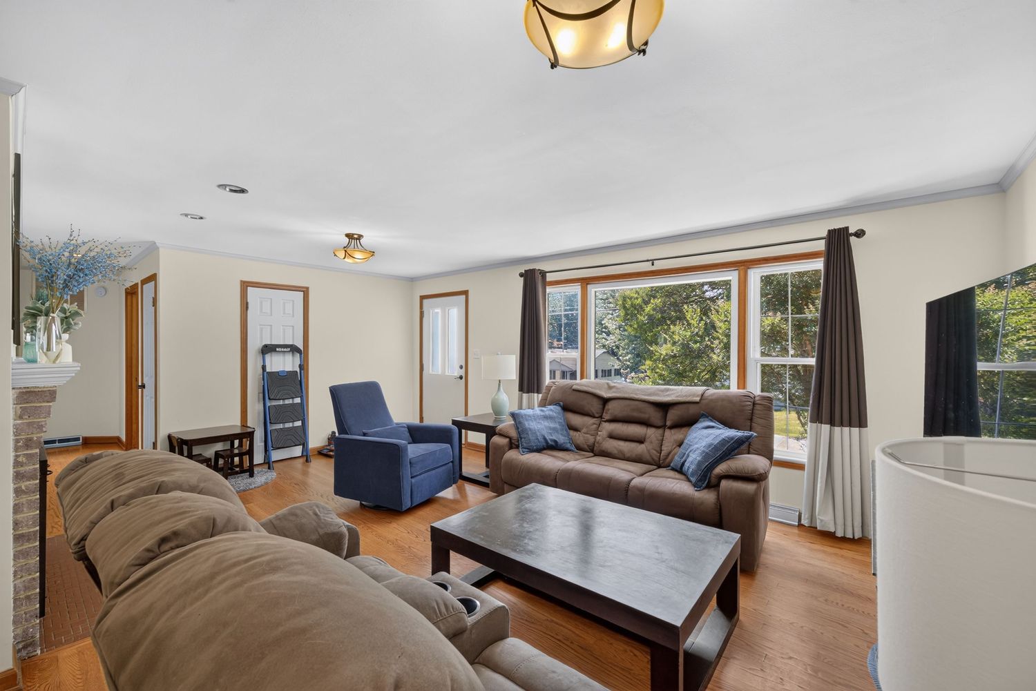 Bright living room with brown sectional sofa, dark wood coffee table, hardwood floors, and large windows with natural light.