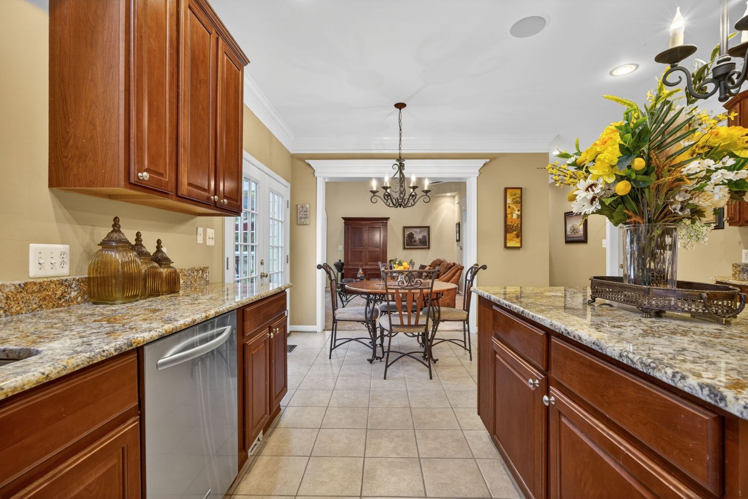 Elegant kitchen with cherry wood cabinets, granite countertops, and a view into a dining area with chandelier.