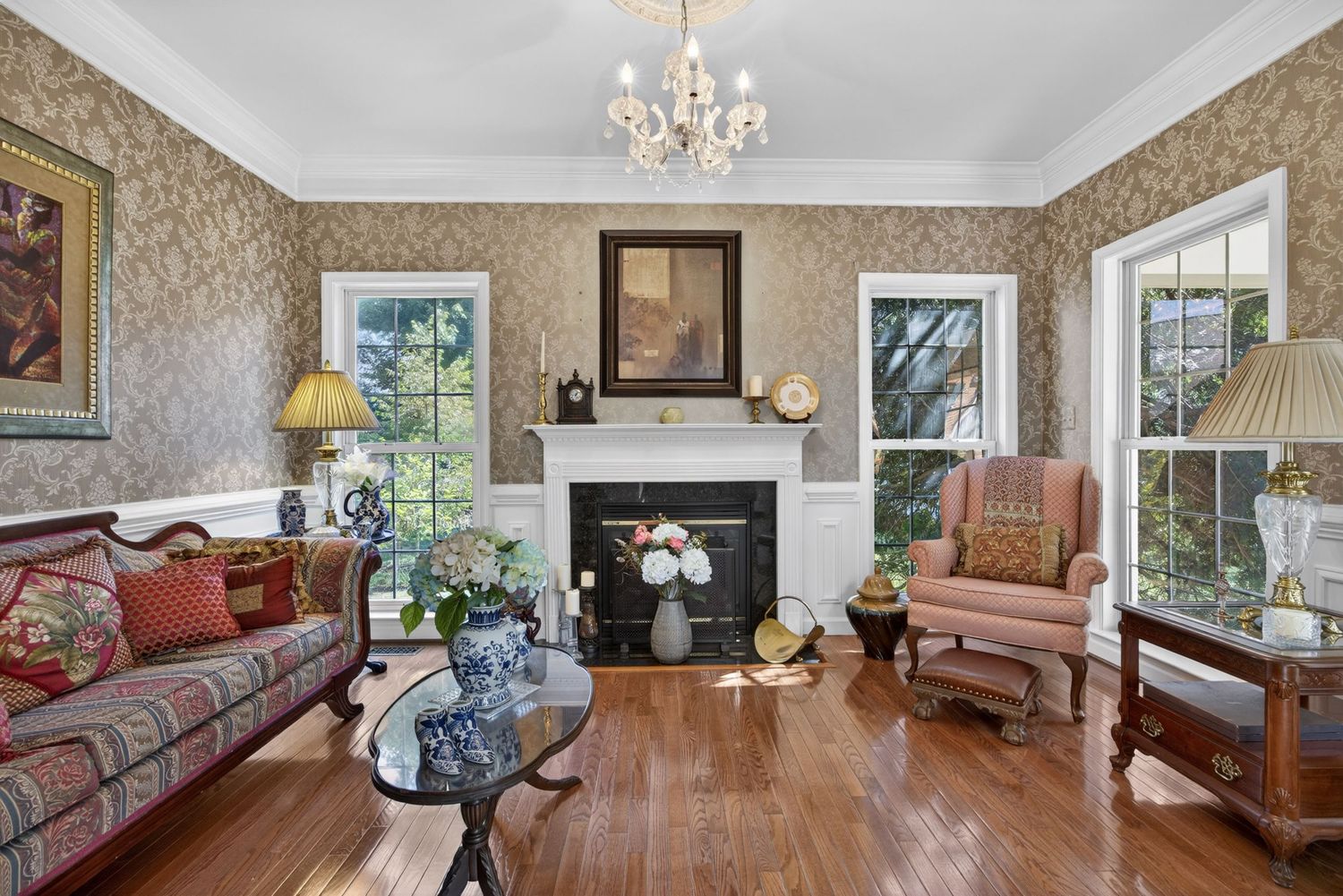 Elegant living room with hardwood floors, ornate wallpaper, fireplace, chandelier, and classic furniture in a traditional style.