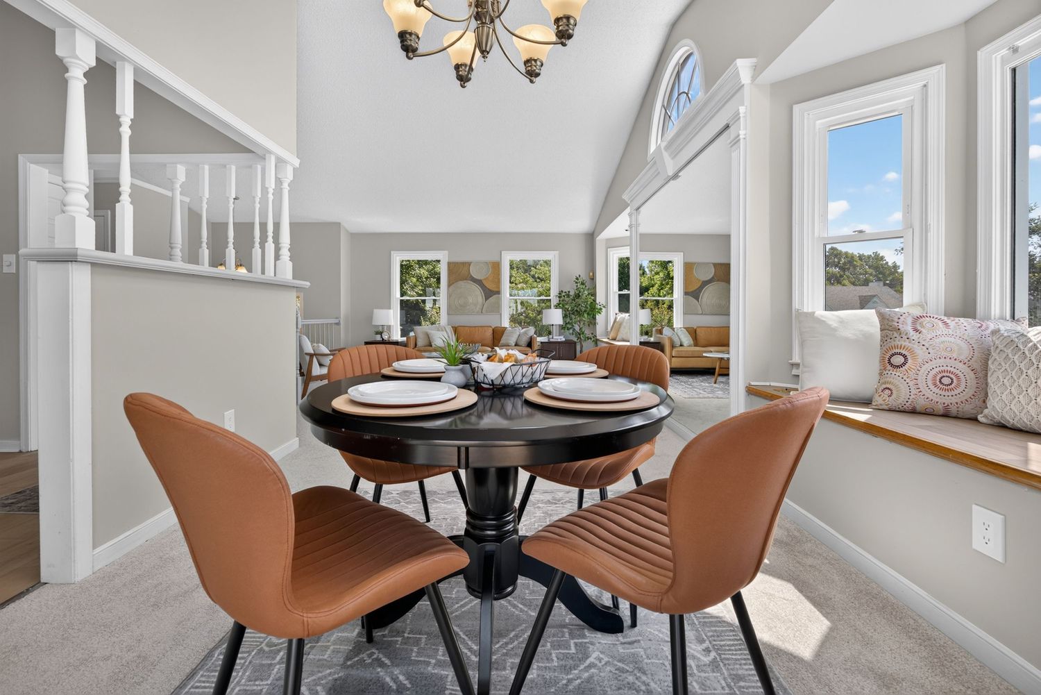 Bright dining room with round black table, brown leather chairs, chandelier, and window seat.
