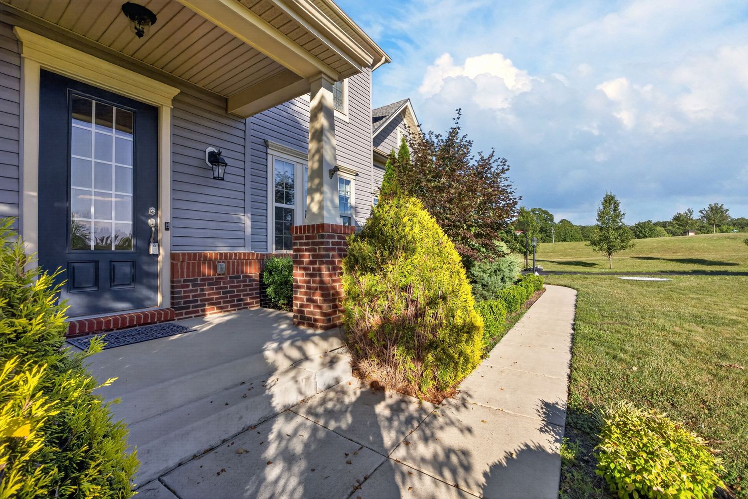 Charming home exterior with brick accents, lush landscaping, and a concrete walkway leading to the front entrance.
