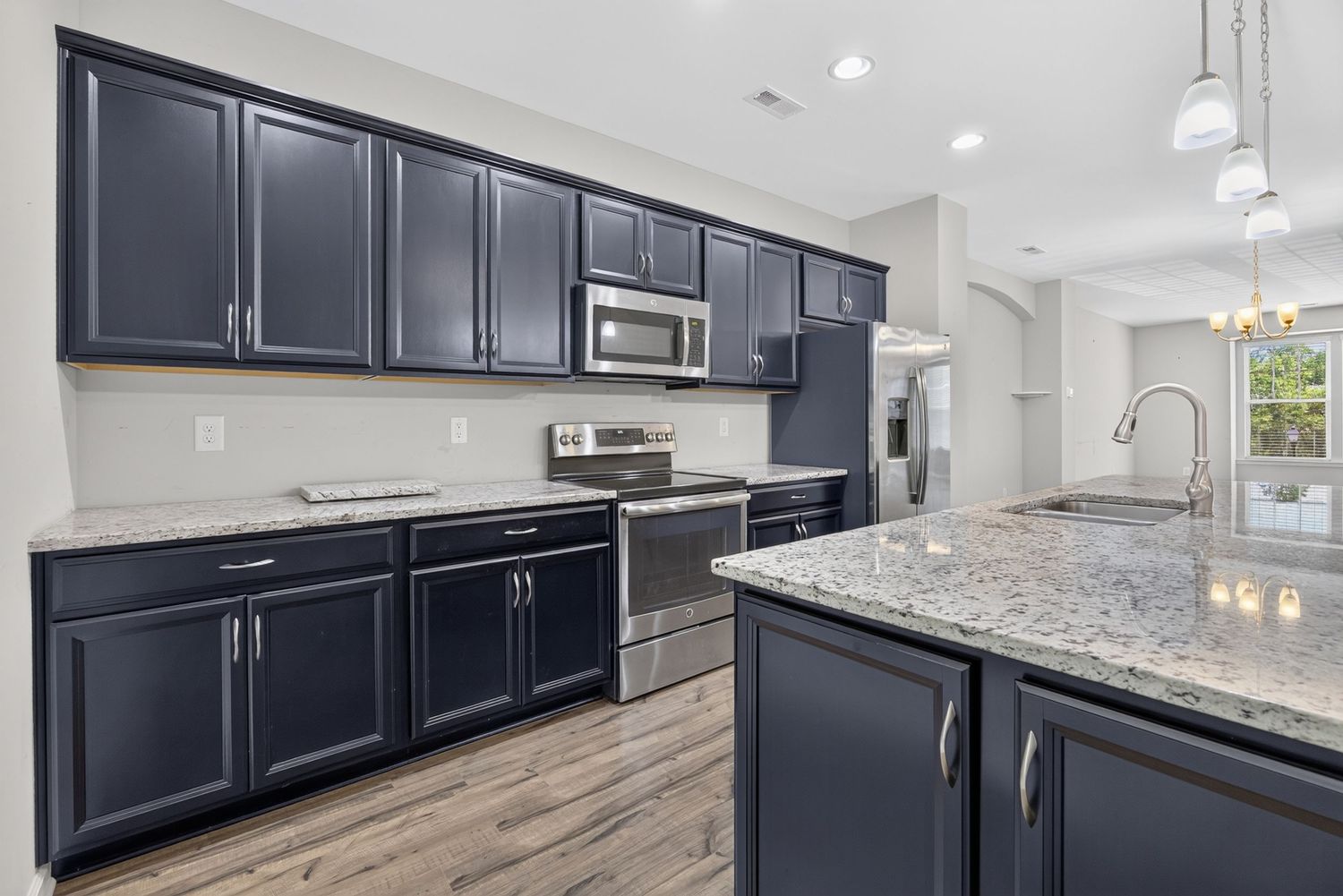 Modern kitchen with navy blue cabinets, granite island, stainless steel appliances, and hardwood floors.