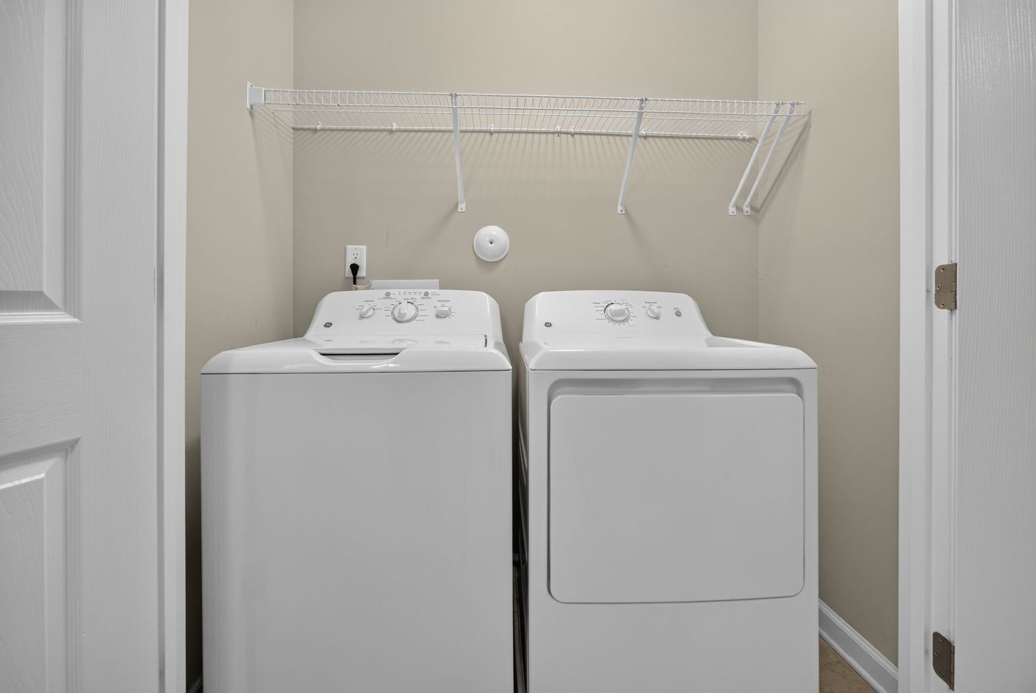 White top-load washer and dryer set in a laundry closet with built-in shelving and hanging rod.