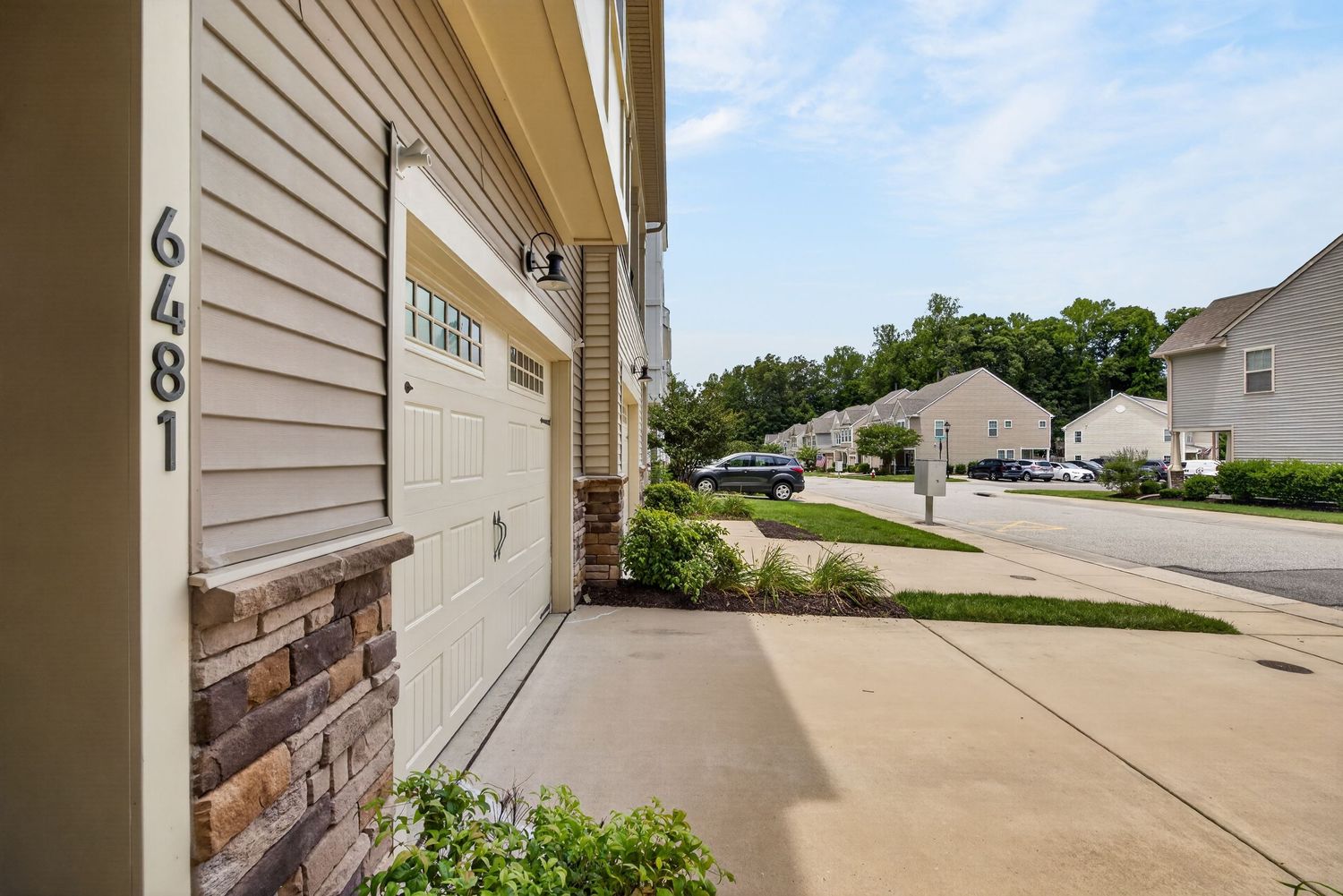 Exterior view of house 6481 with white garage door, stone accents, and a quiet suburban street on a sunny day.