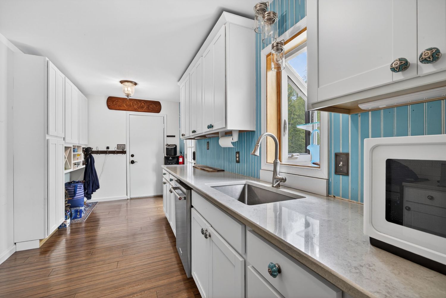 Modern kitchen with white cabinets, granite countertops, stainless steel sink, and blue tile backsplash with hardwood floors.