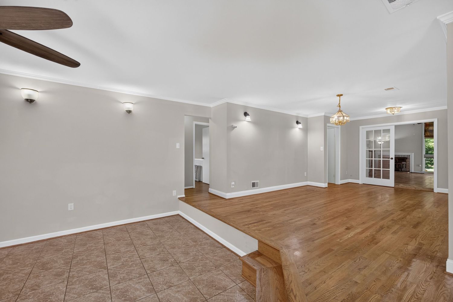 Spacious open-concept living area with hardwood floors, tile entryway, crown molding, ceiling fan, and French doors leading to another room.