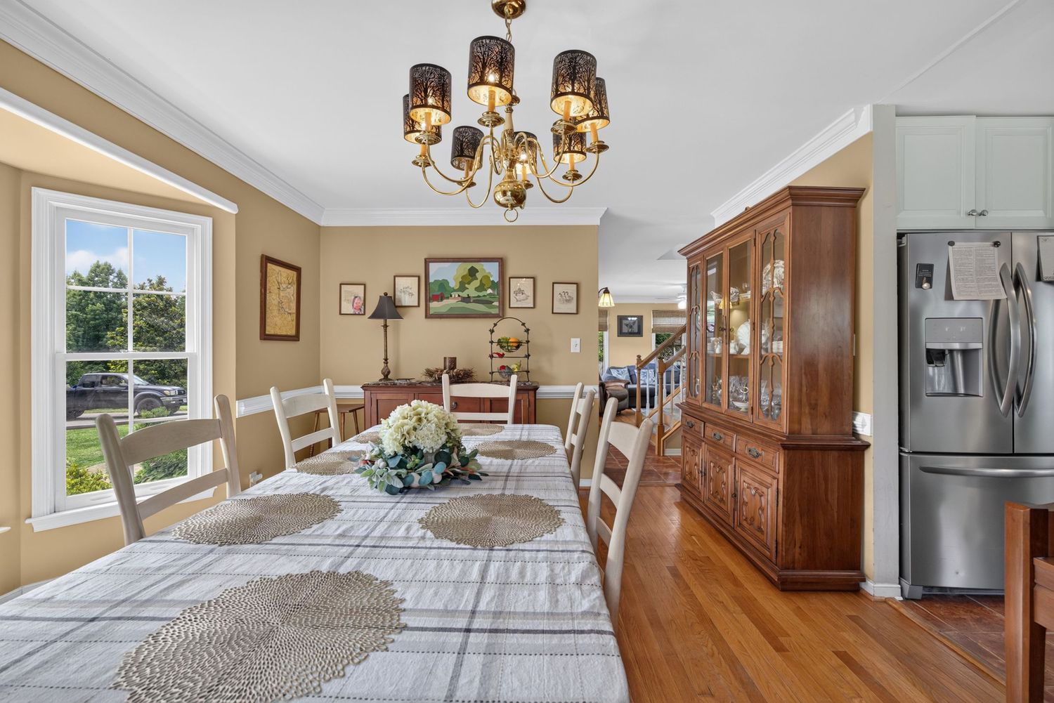 Elegant dining room with hardwood floors, white chair rail, chandelier, china cabinet, and seating for eight near bright windows.