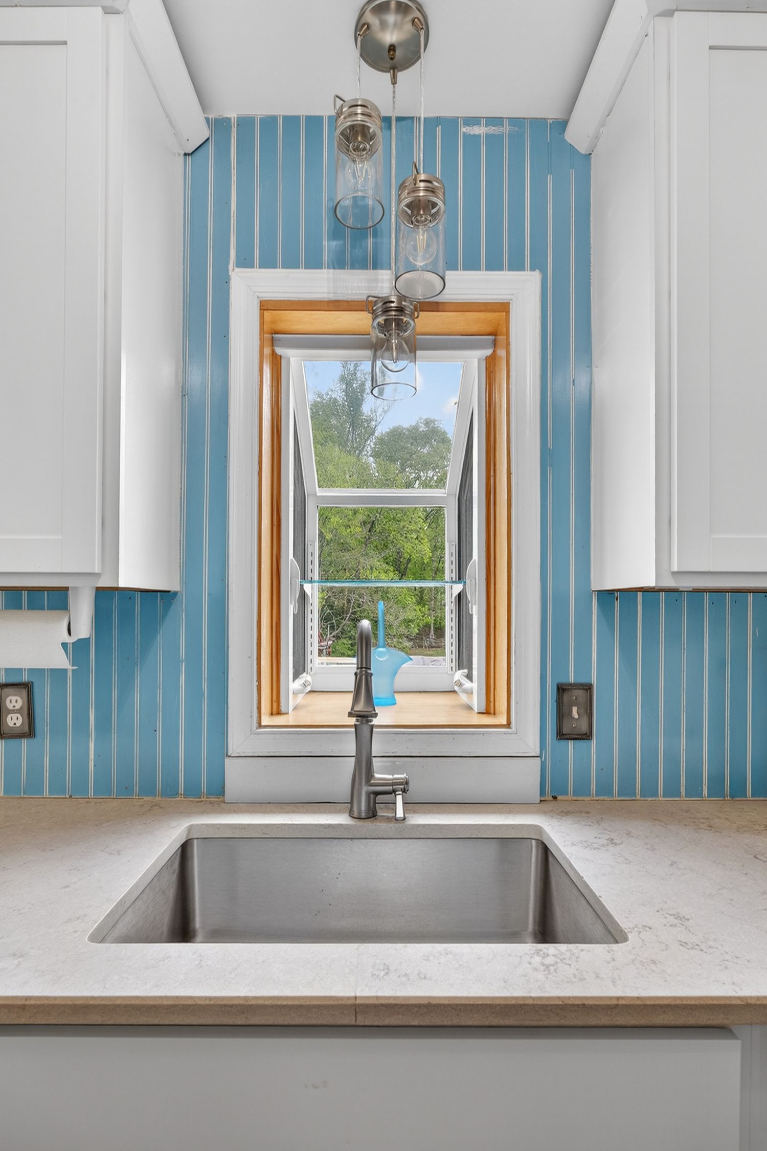 Modern kitchen sink with stainless steel faucet, marble countertop, and blue tile backsplash framing a bright window.