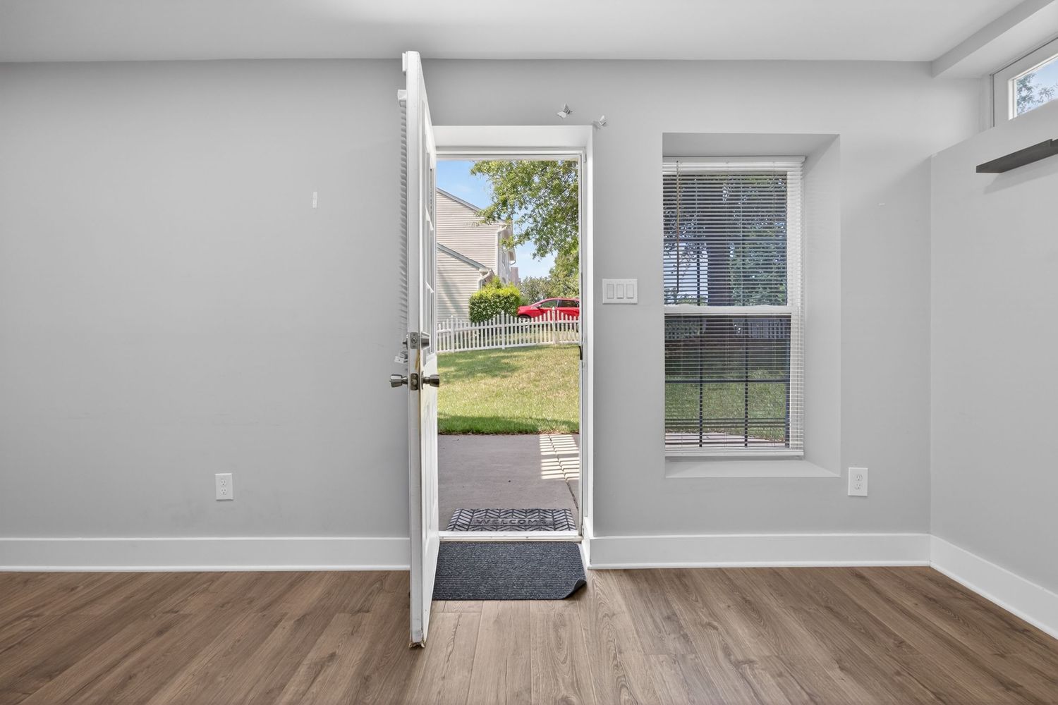 Bright entryway with open door leading to green yard, wood floors, gray walls, and a white window.