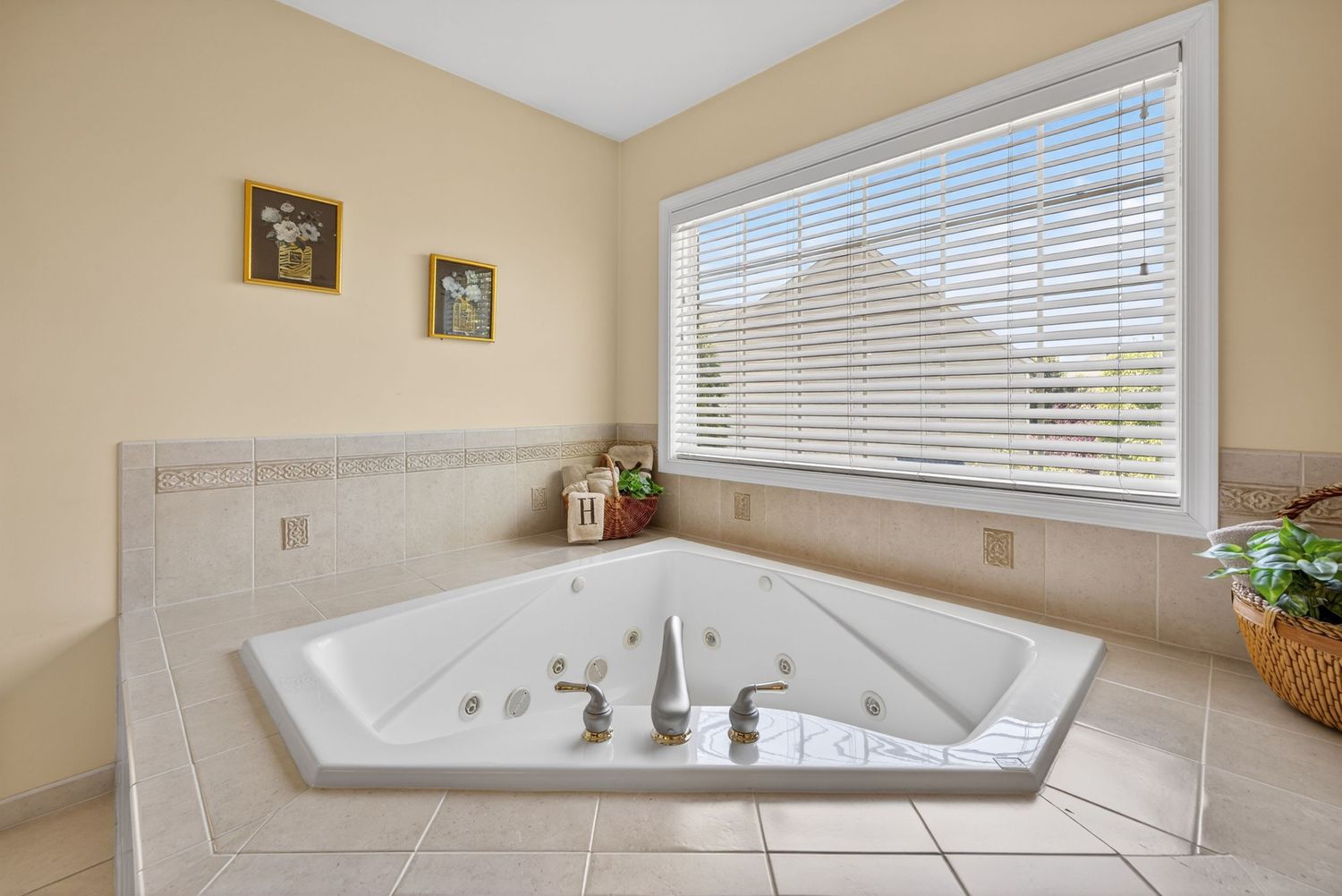 Corner jetted soaking tub with tile surround and large window in a bright, neutral-toned master bathroom.