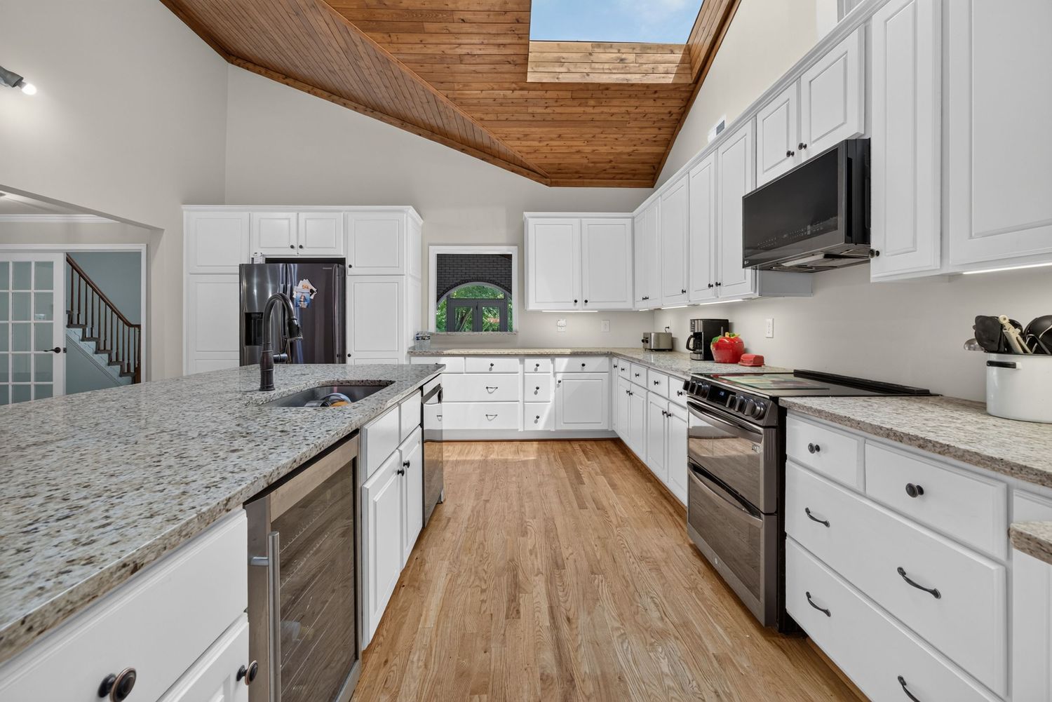 Modern kitchen with white cabinets, granite countertops, stainless steel appliances, hardwood floors, and vaulted wood ceiling.
