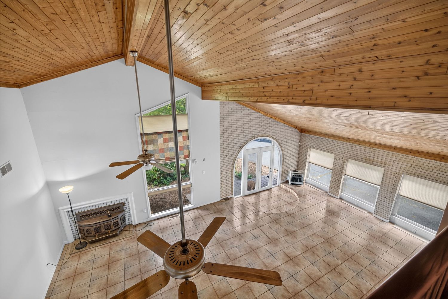 Bright living room with vaulted wood ceiling, ceiling fan, arched doorway, and large windows with tile flooring.