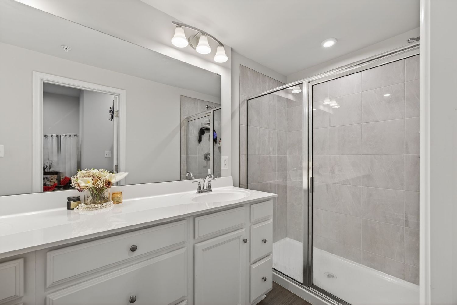 Modern bathroom with white vanity, large mirror, and glass-enclosed marble tile shower stall.