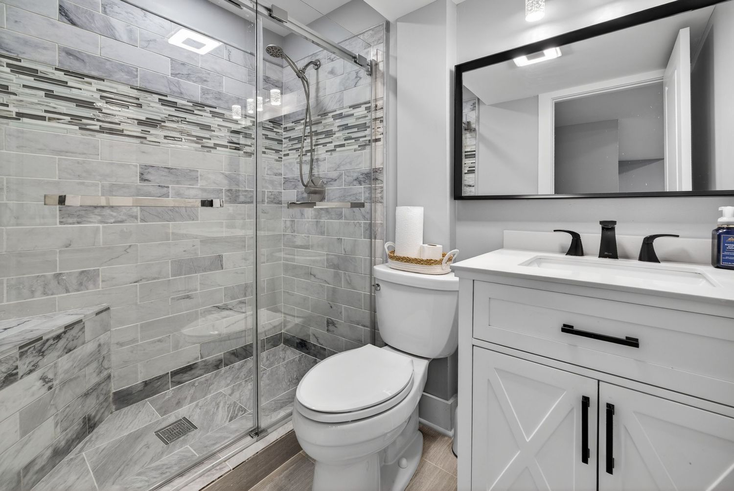 Modern bathroom with glass walk-in shower, marble tile walls, white vanity, black fixtures, and toilet.