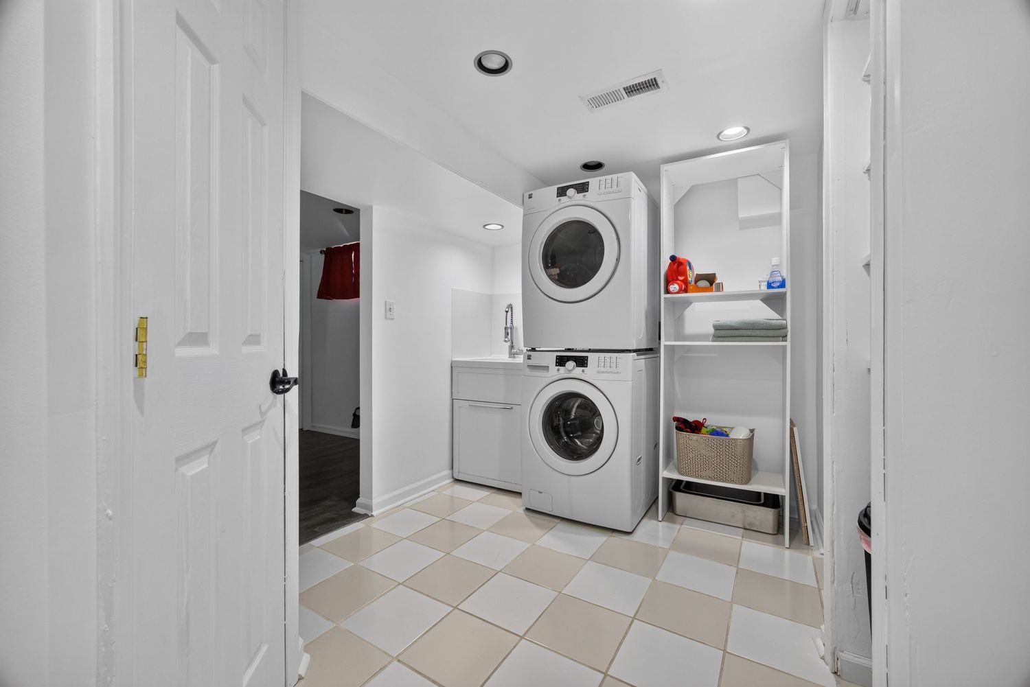 Bright laundry room with stacked and standalone white washer and dryer units, checkered tile flooring, and white walls.
