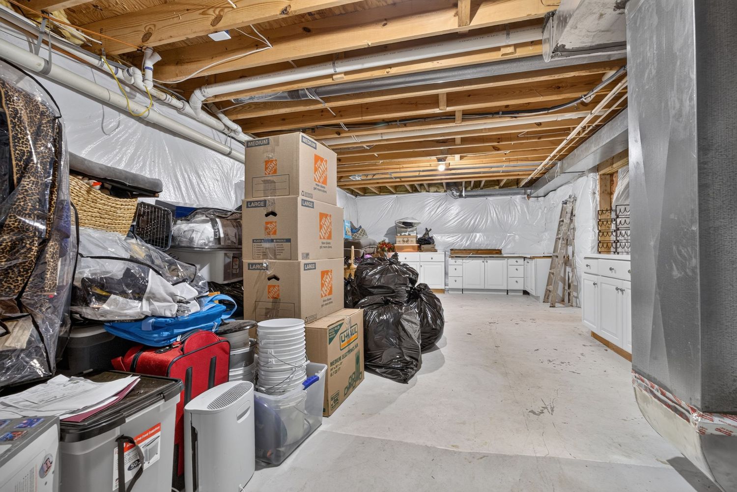 Unfinished basement storage area with exposed ceiling joists, cardboard boxes, and concrete floors.