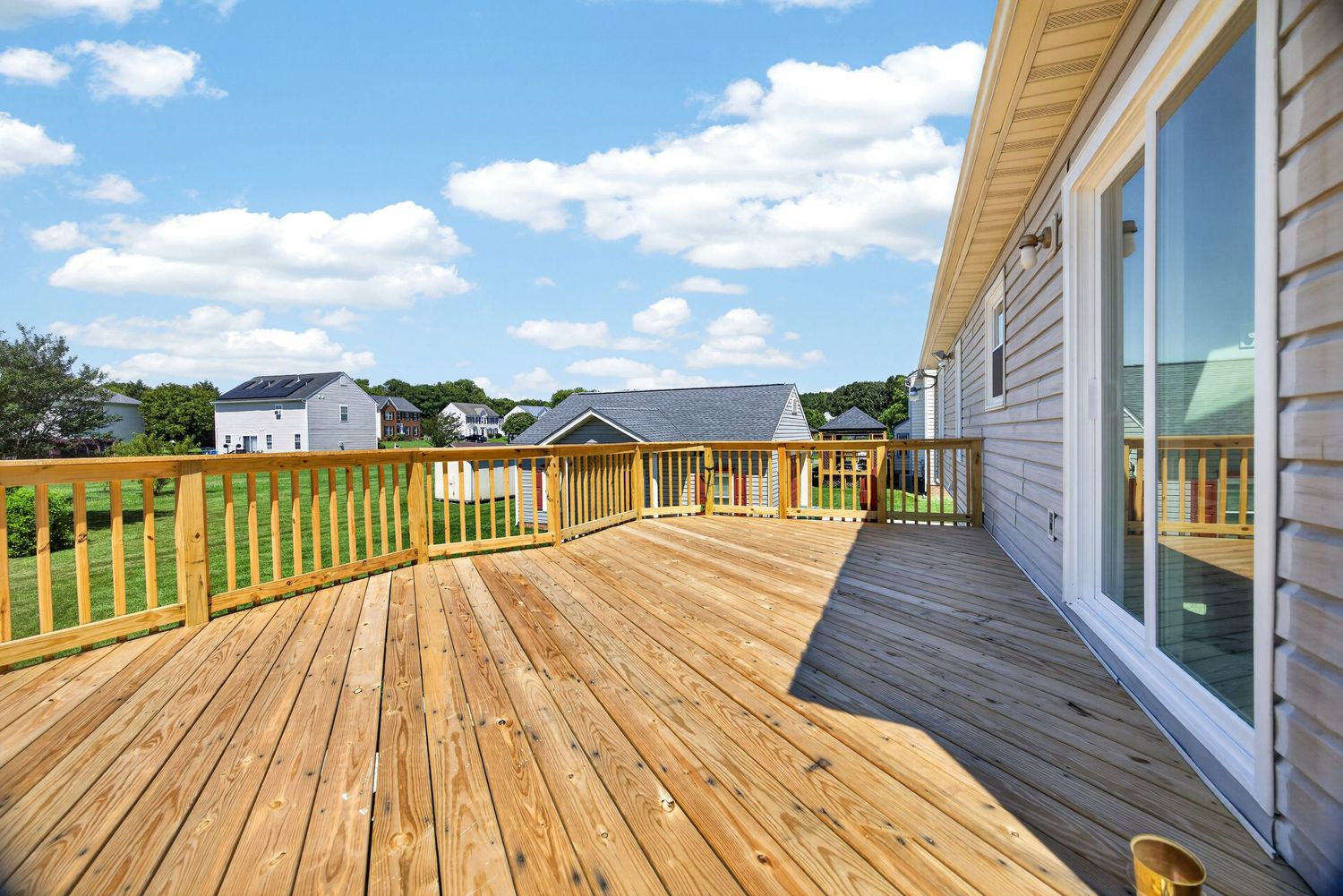 Spacious wooden deck with light pine boards, green railing, and sliding glass door overlooking a suburban neighborhood.