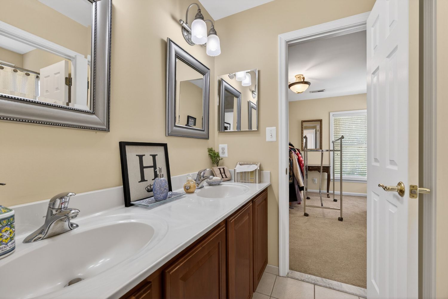 Elegant bathroom with double sink vanity, dark wood cabinets, marble countertop, dual mirrors, and a view into a walk-in closet.