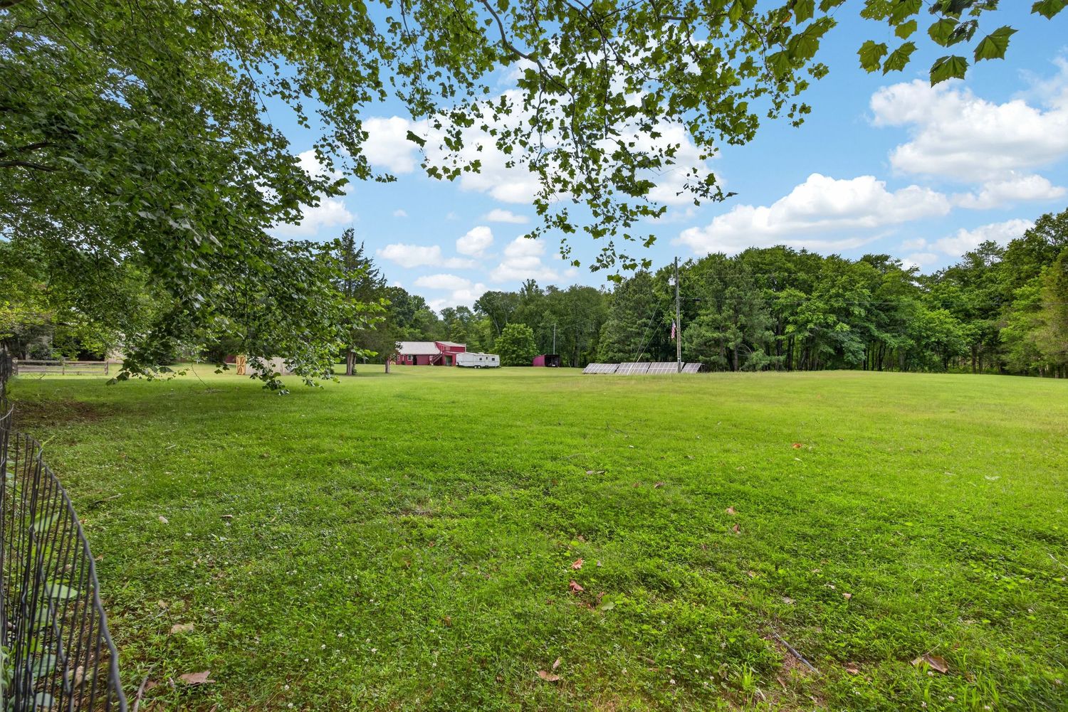 Expansive green lawn surrounded by tall trees with a red barn visible in the background under a partly cloudy sky.