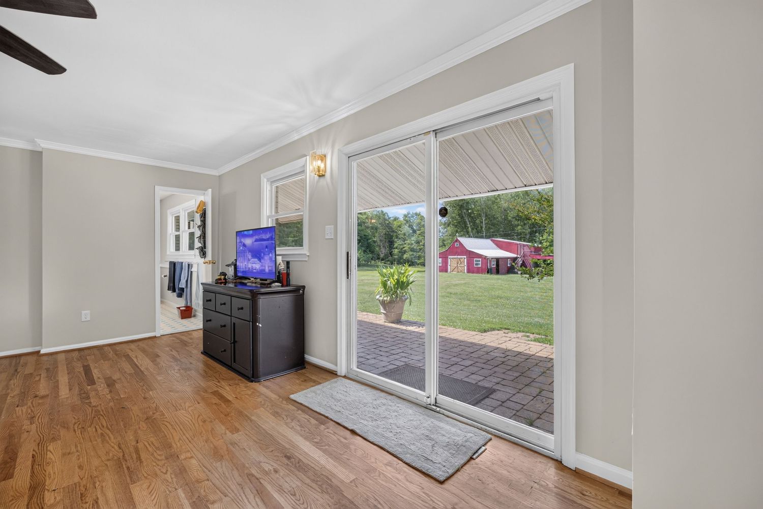 Bright living room with hardwood floors, crown molding, sliding glass doors opening to a patio with a red barn view.