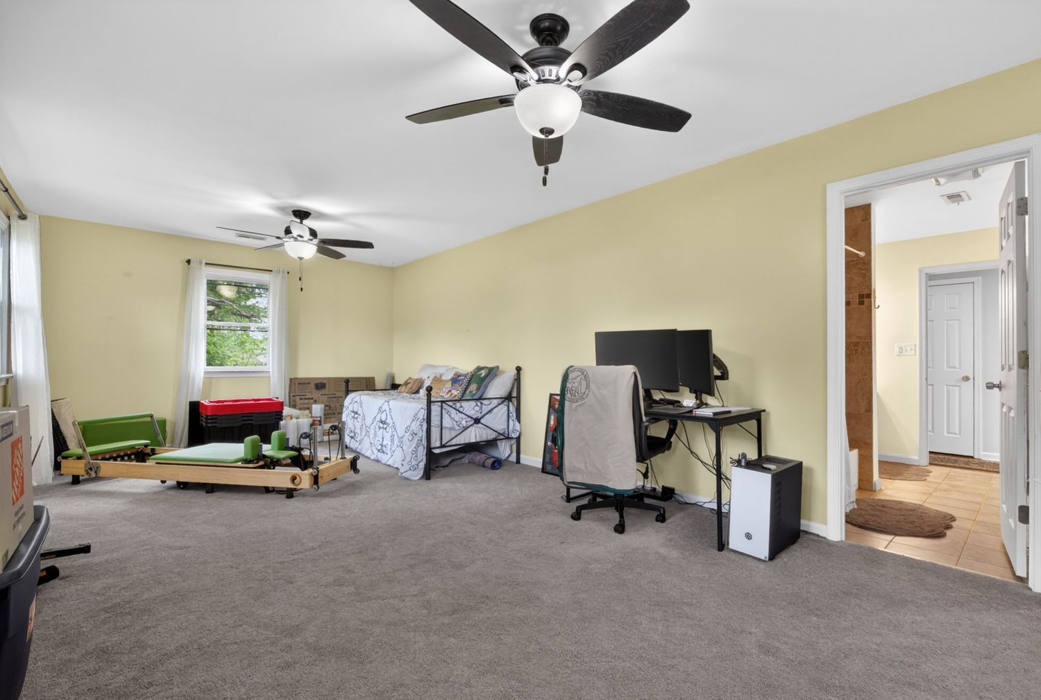 Spacious bedroom with gray carpet, ceiling fan, computer desk, and natural light from window.