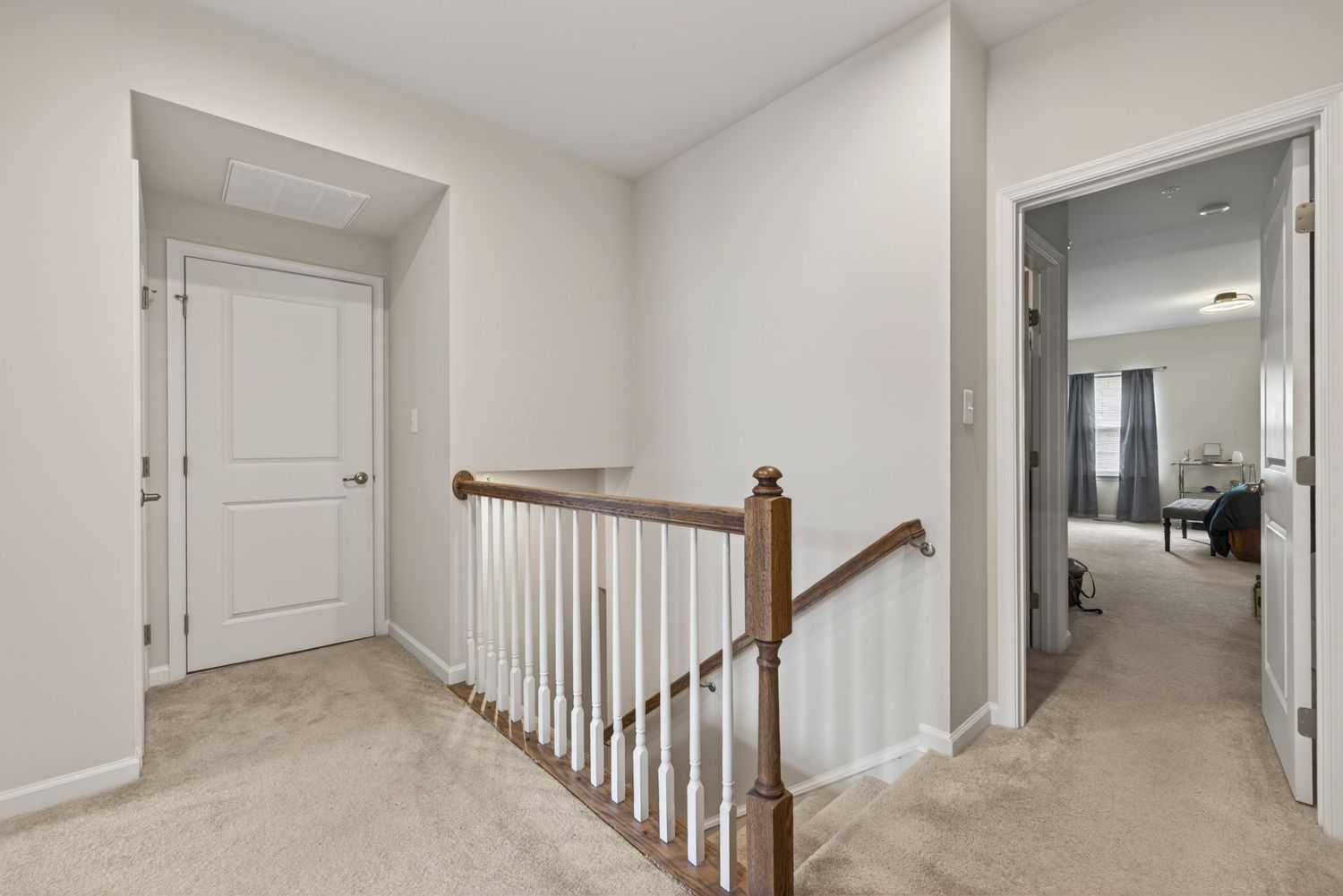 Bright hallway with carpeted floors, white staircase railing, and white paneled doors in a modern home.