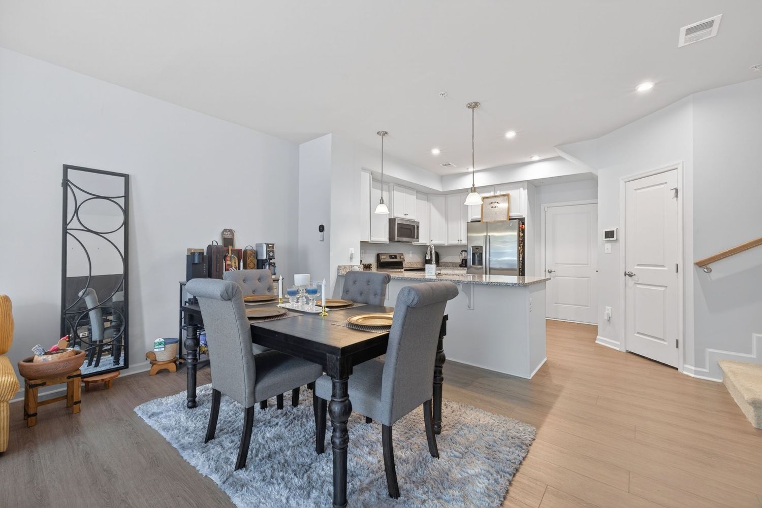 Open-concept dining area with gray chairs, wood floors, and modern white kitchen with stainless steel appliances.