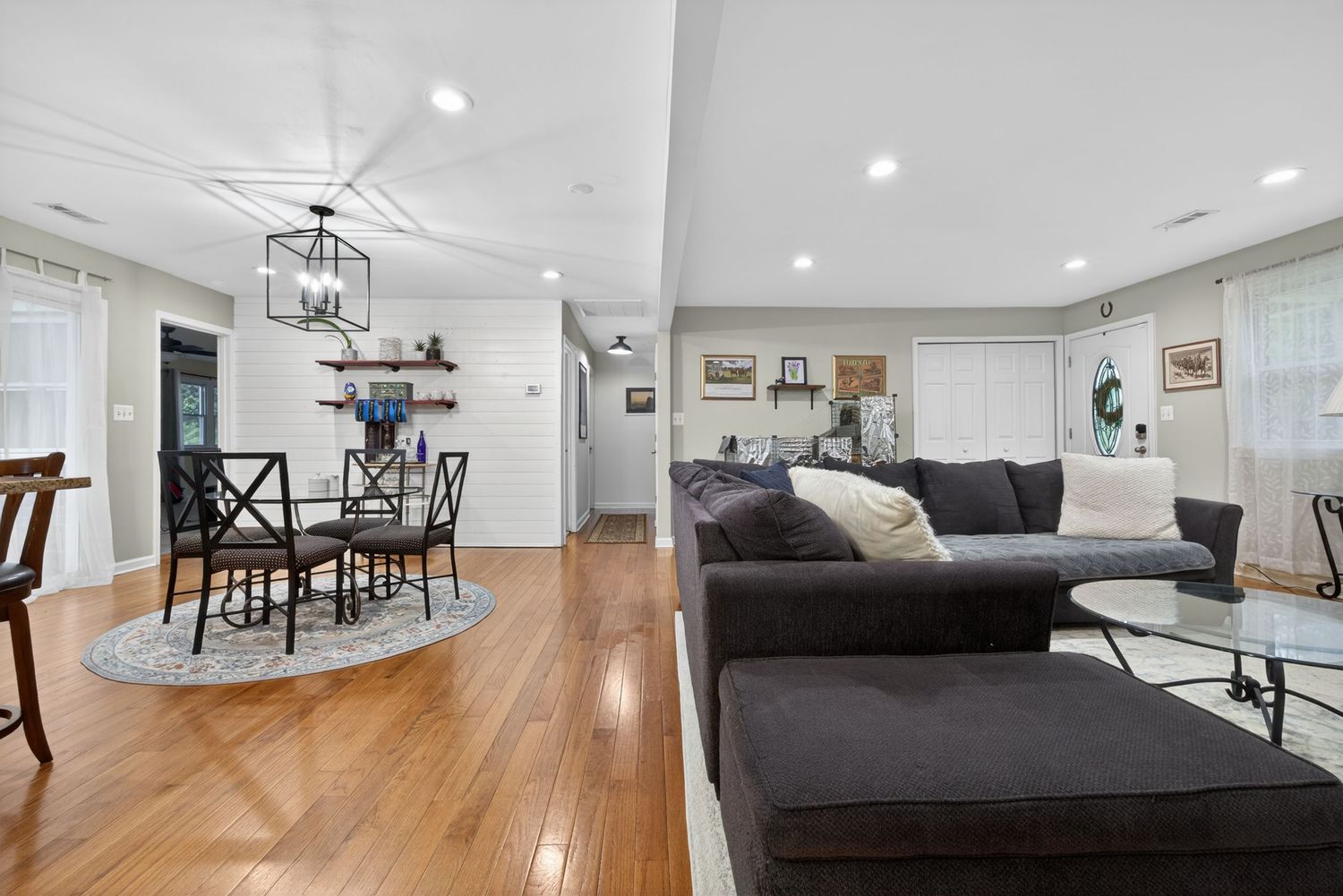 Open-concept living room with hardwood floors, dark sectional sofa, and dining area with chandelier.