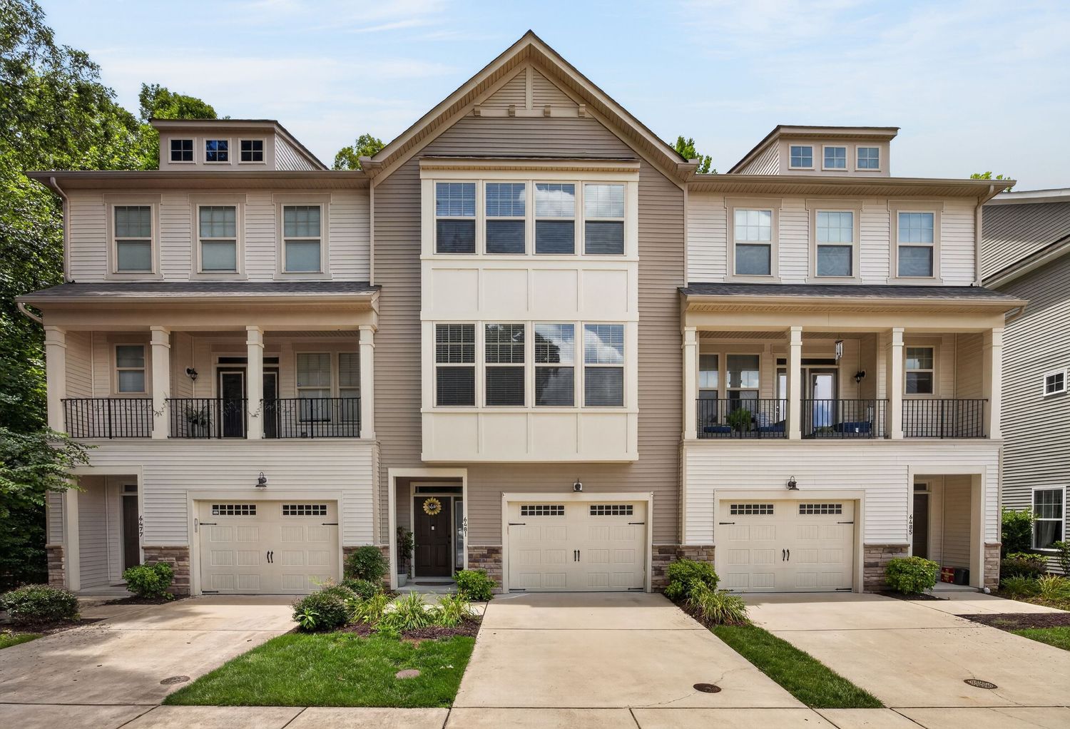 Three-story townhome with beige exterior, white trim, two-car garage, and covered balconies in a residential community.