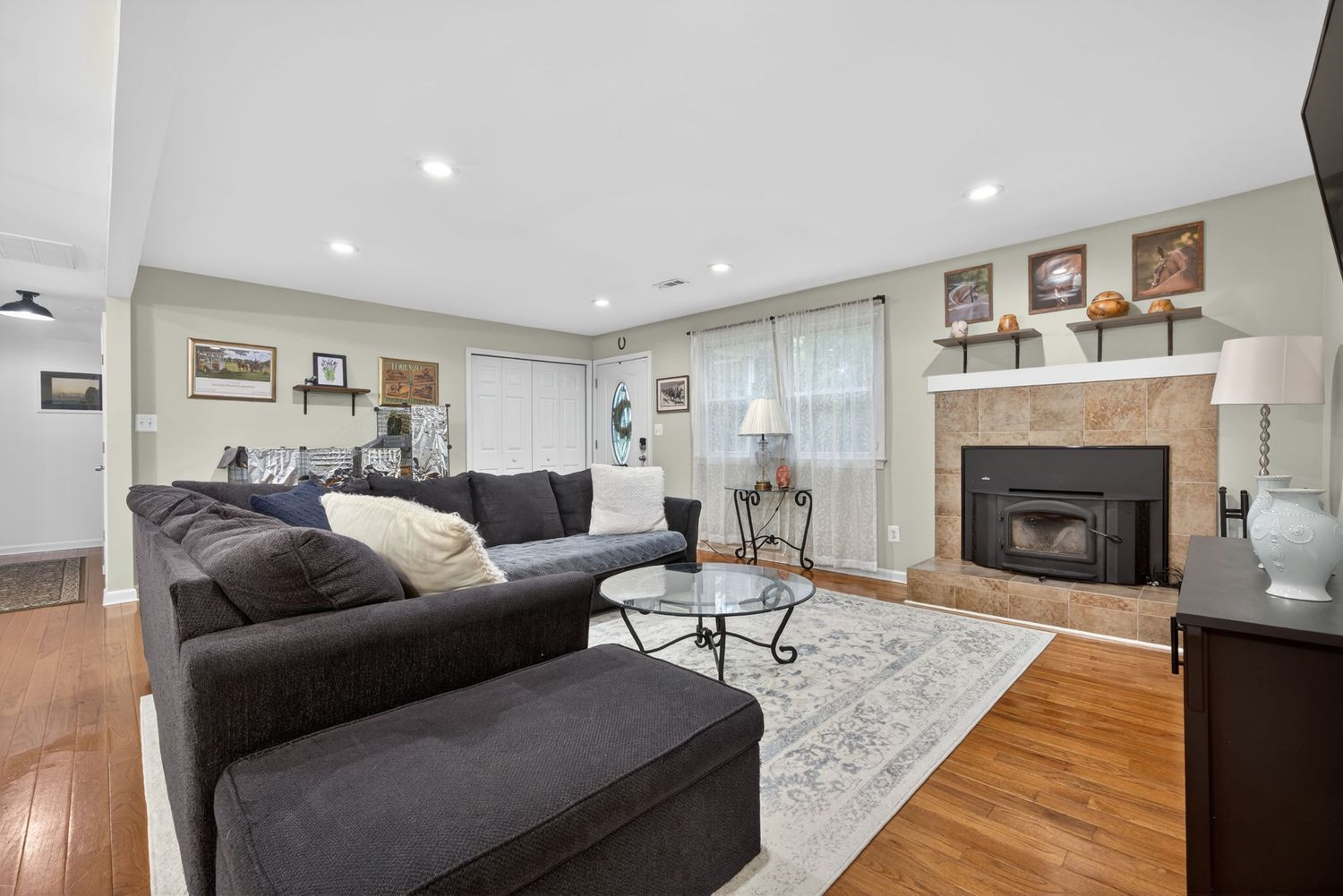 Bright living room with dark sectional sofa, glass coffee table, hardwood floors, and a tiled fireplace with built-in shelving.