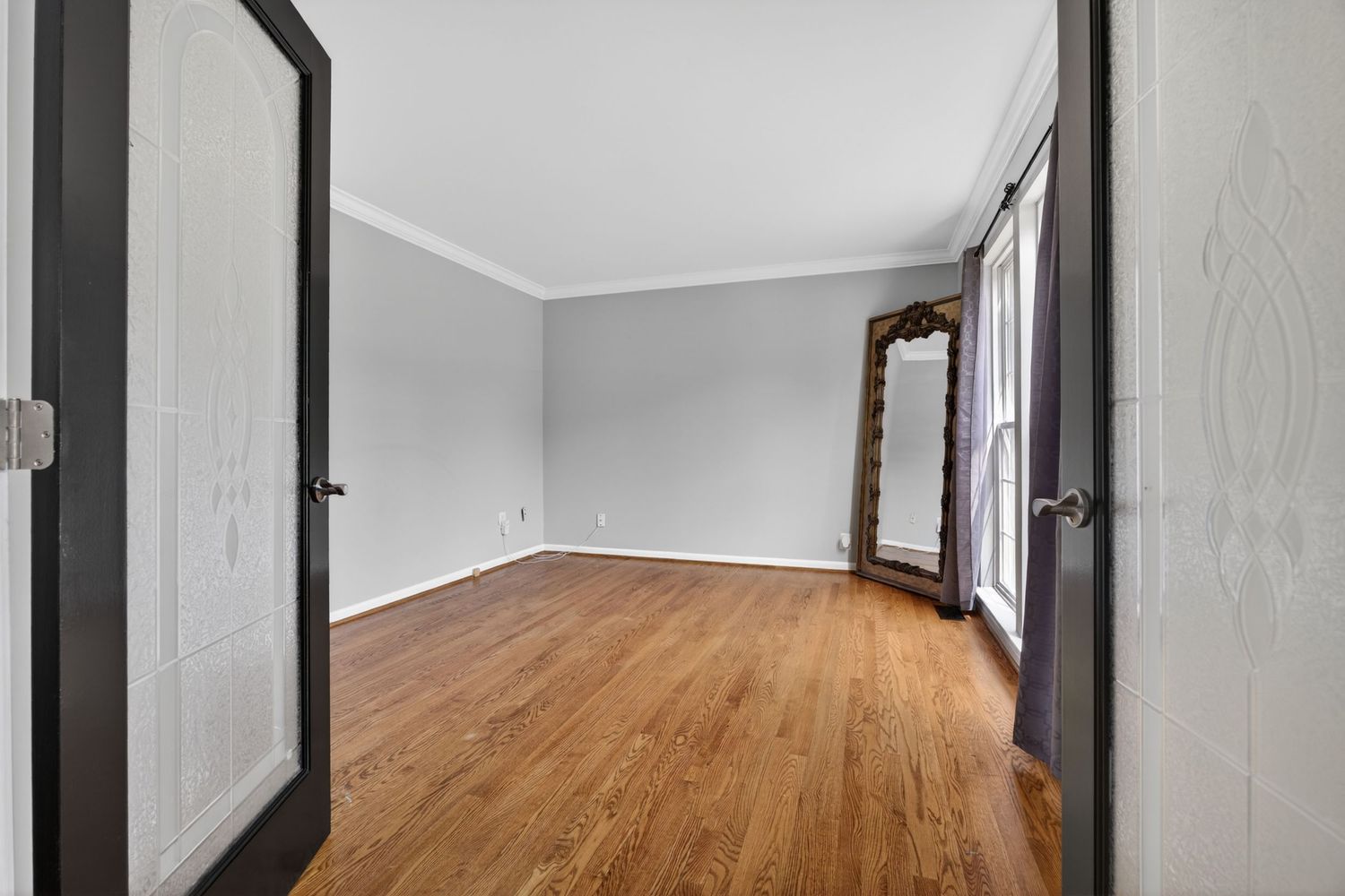 Empty room with hardwood floors, white walls, crown molding, and French doors letting in natural light.