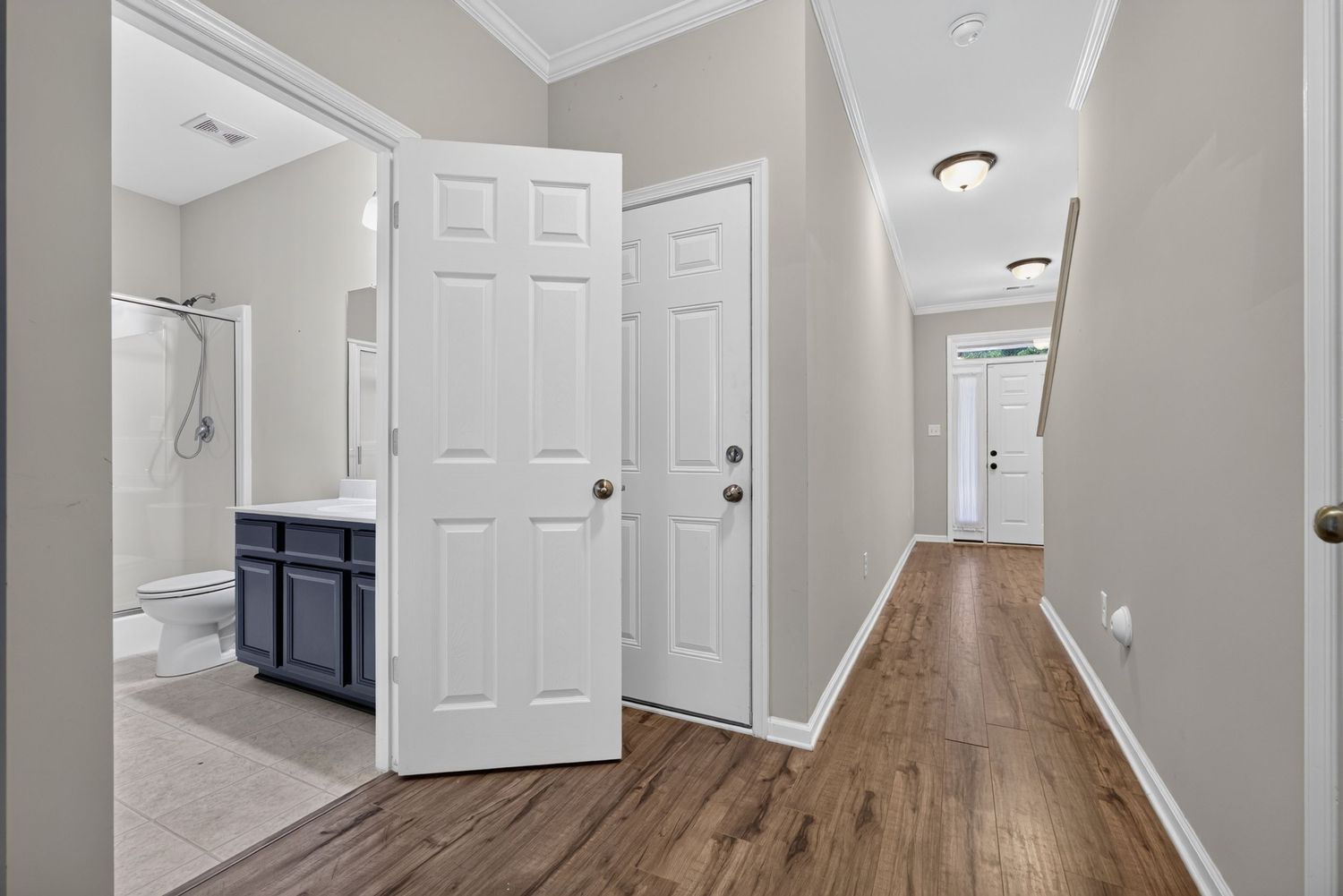 Hallway with hardwood floors, crown molding, white doors, and a view into a bathroom with dark vanity.