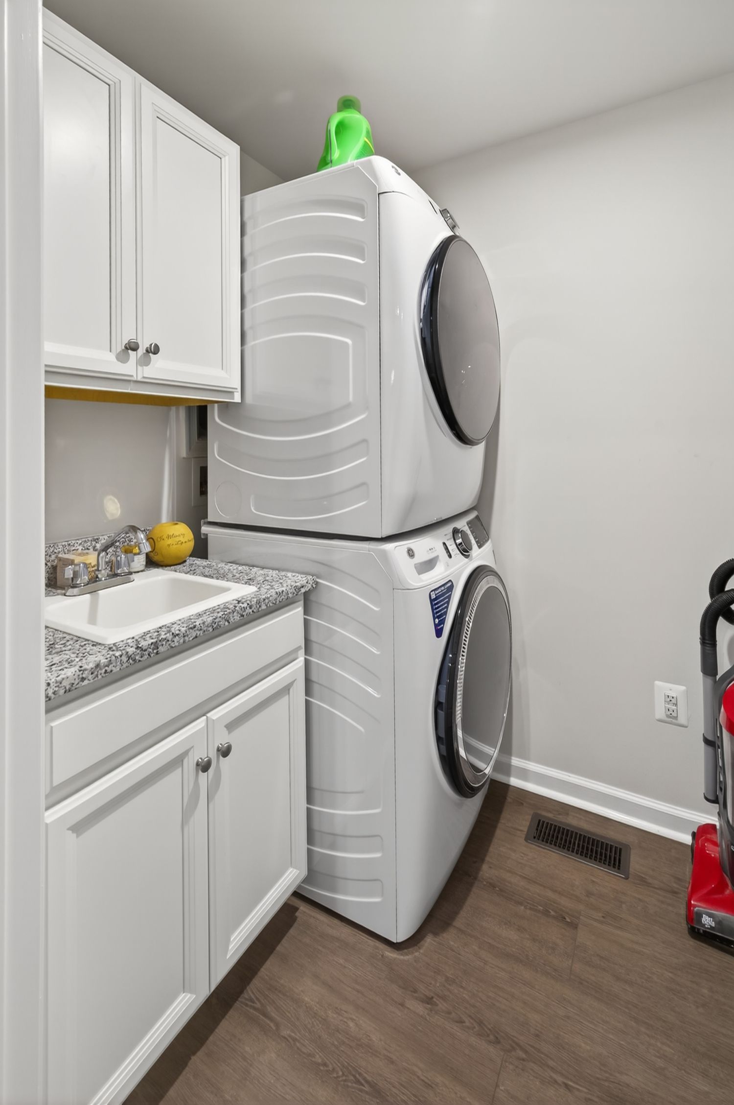 Laundry room with stacked white washer and dryer, white cabinets, granite countertop, and hardwood floors.