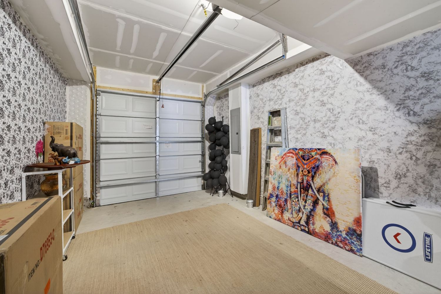 Spacious garage interior with decorative wallpaper, wooden flooring, and colorful elephant artwork near the garage door.