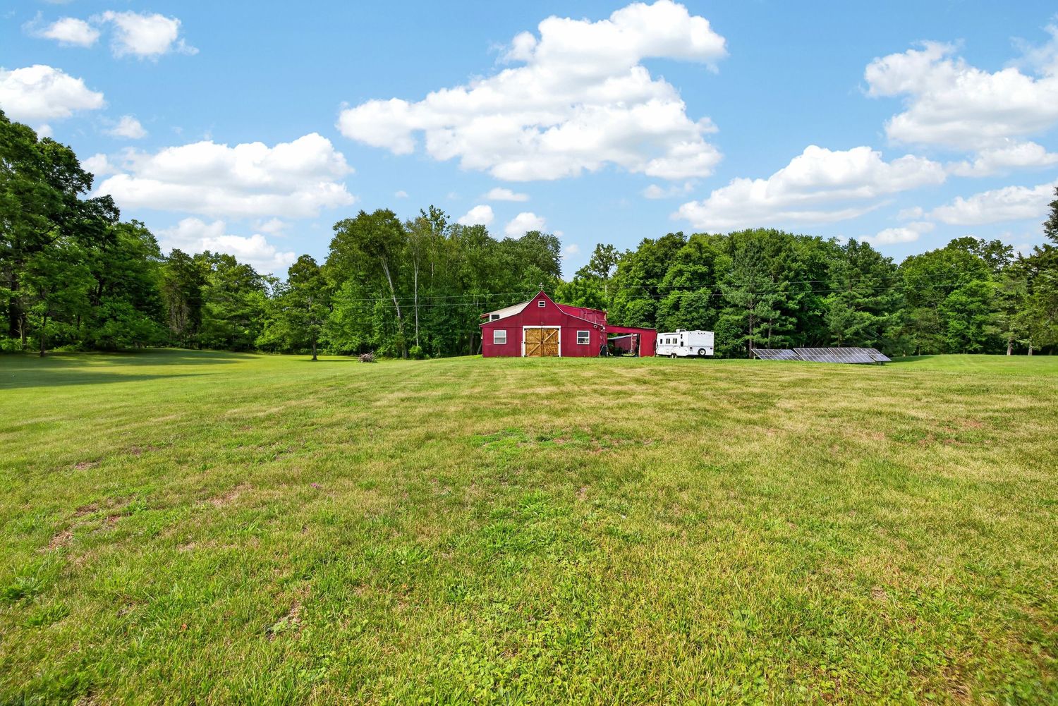 Red barn surrounded by lush green trees on a spacious rural property with a wide open grassy lawn.