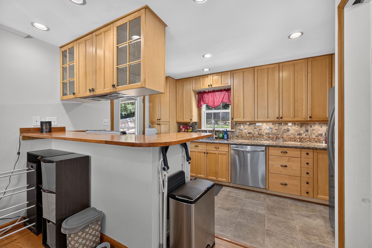 Modern kitchen with light wood cabinets, granite counters, stainless steel appliances, and a breakfast bar with tile flooring.